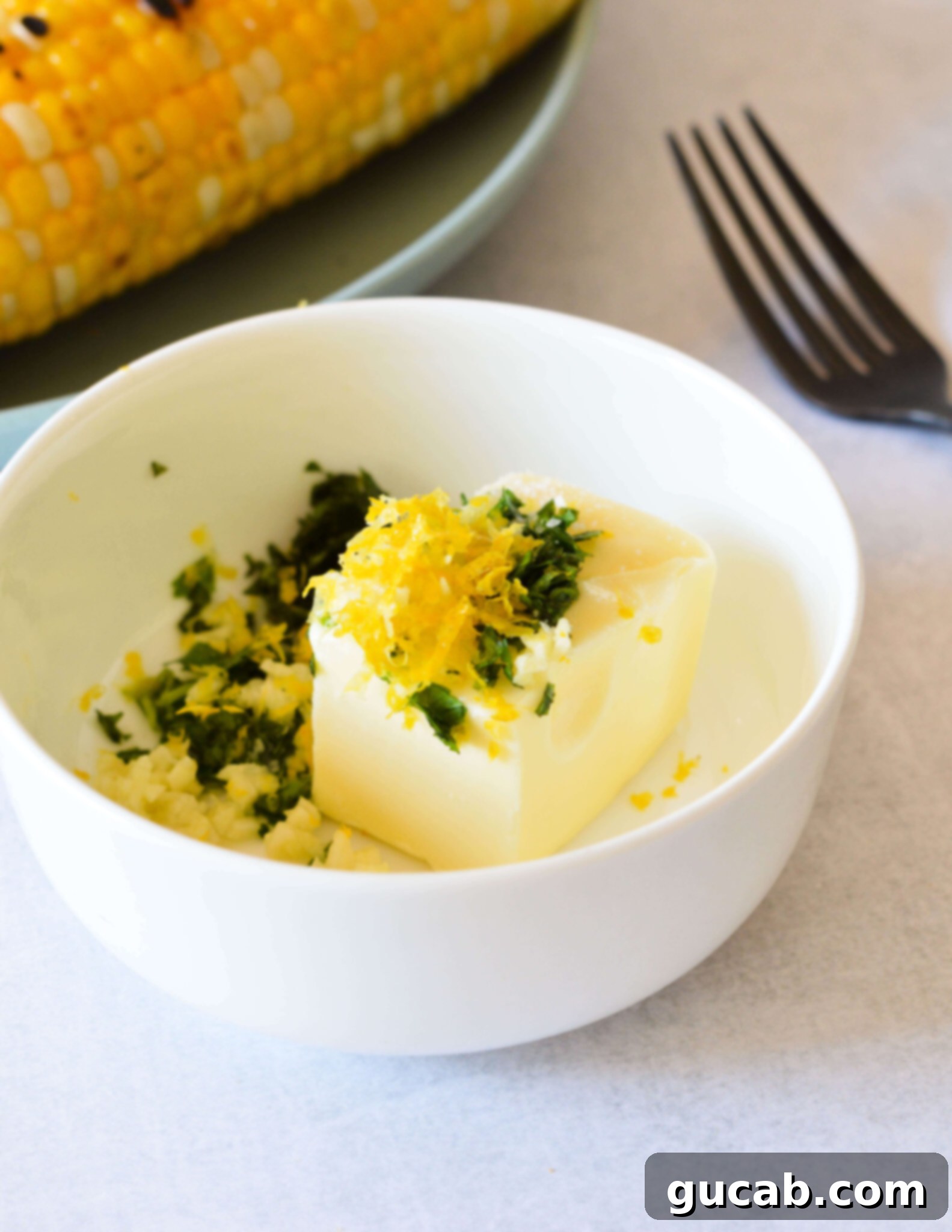 Softened butter, bright yellow lemon zest, and vibrant green fresh herbs placed in a small mixing bowl, ready to be combined.