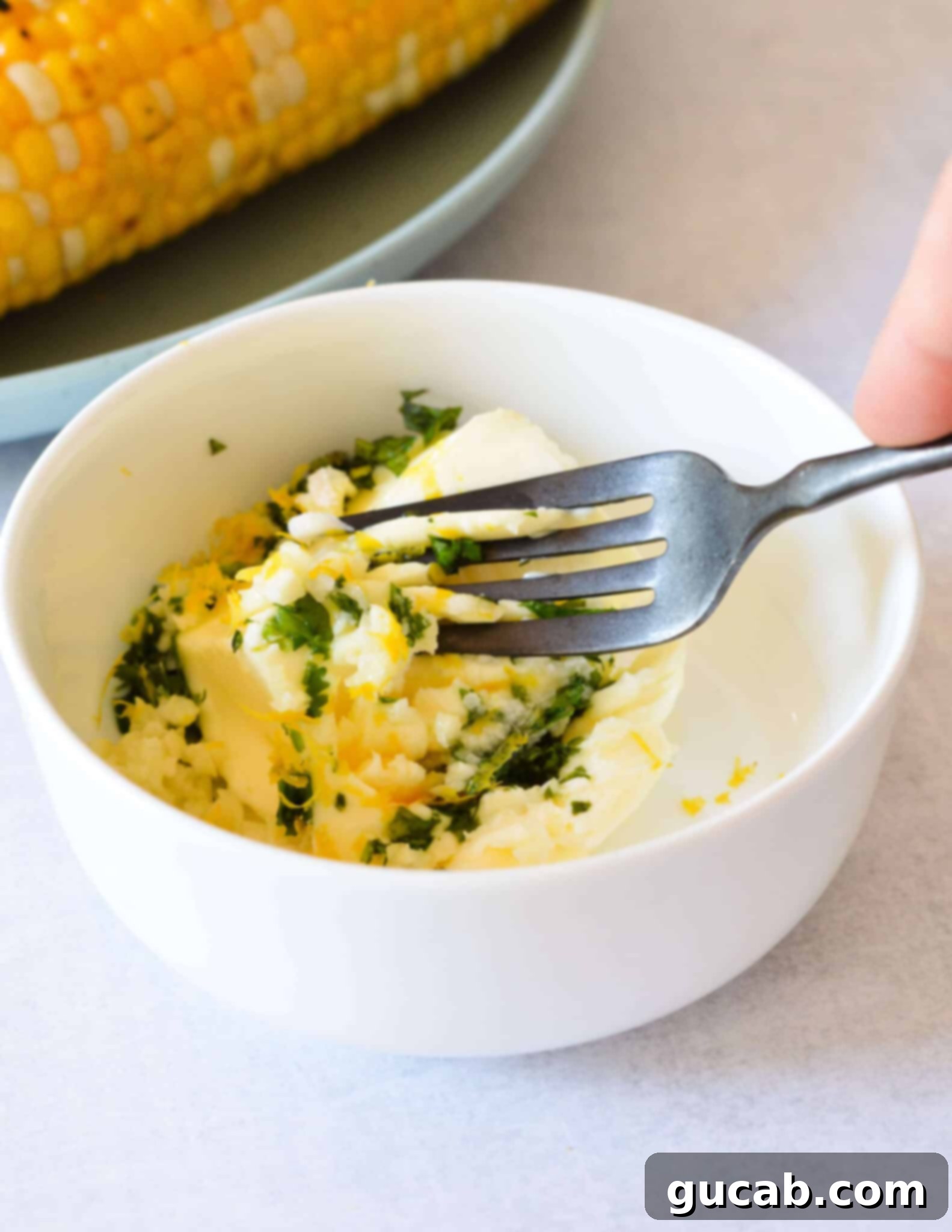 A fork actively mixing softened butter with lemon zest and fresh herbs in a small bowl, creating the lemon herb butter mixture.