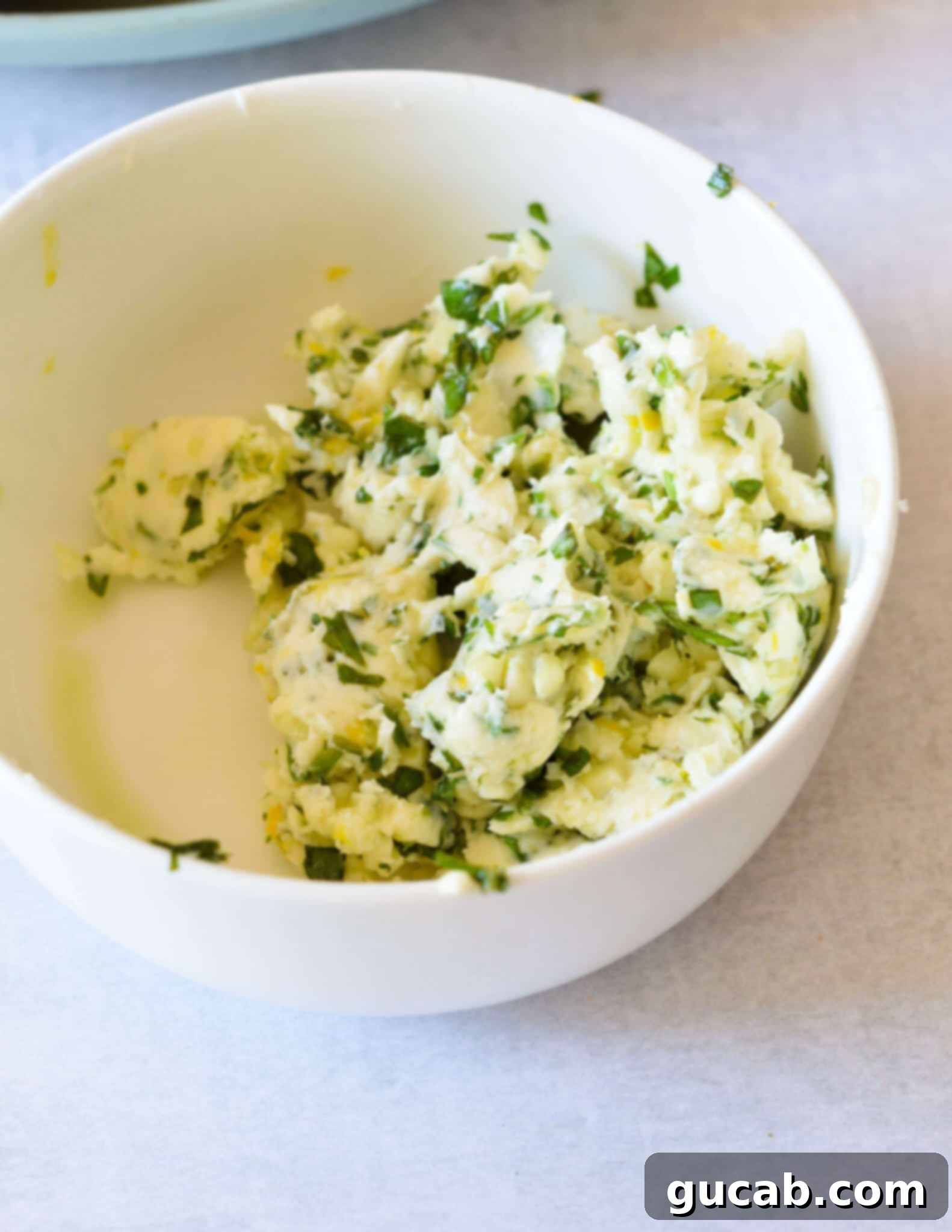 A small bowl filled with the finished, creamy lemon herb butter, ready to be spread on grilled corn.