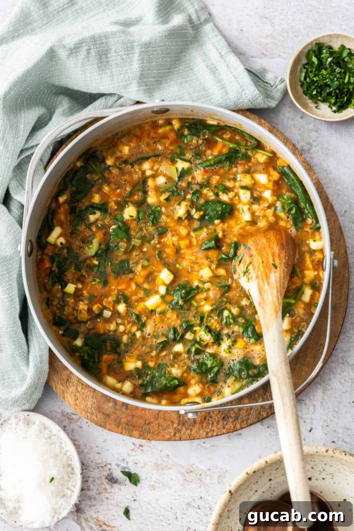 A pot of vibrant Mediterranean red lentil soup, with wilted greens and a rich broth.
