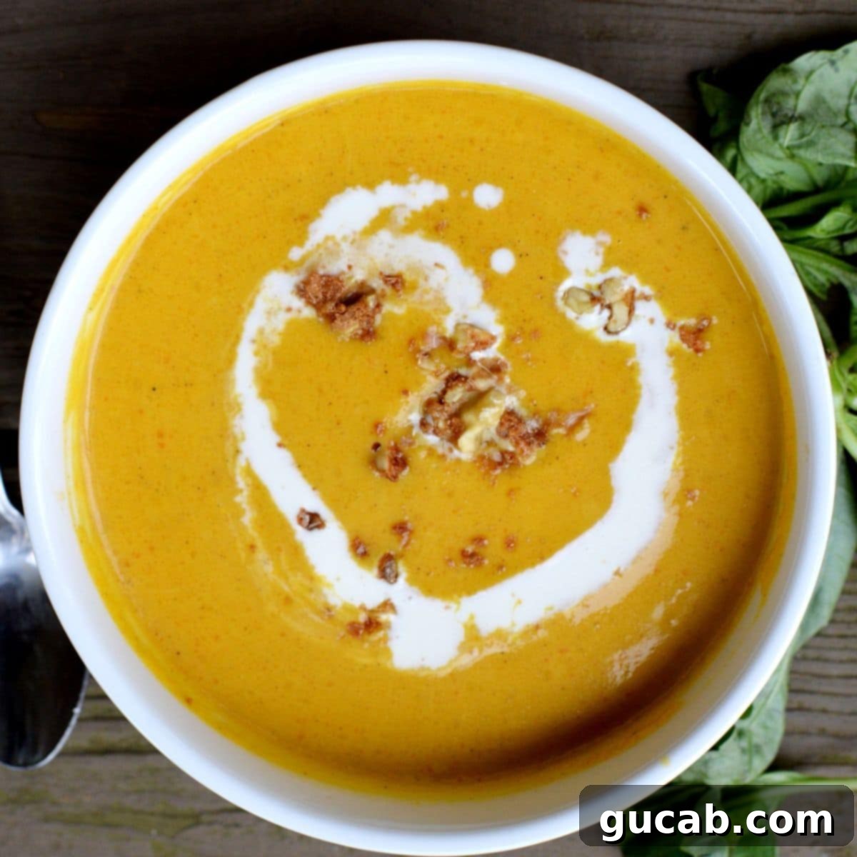 A bowl of creamy butternut squash soup, garnished with a swirl of cream and fresh sage leaves.