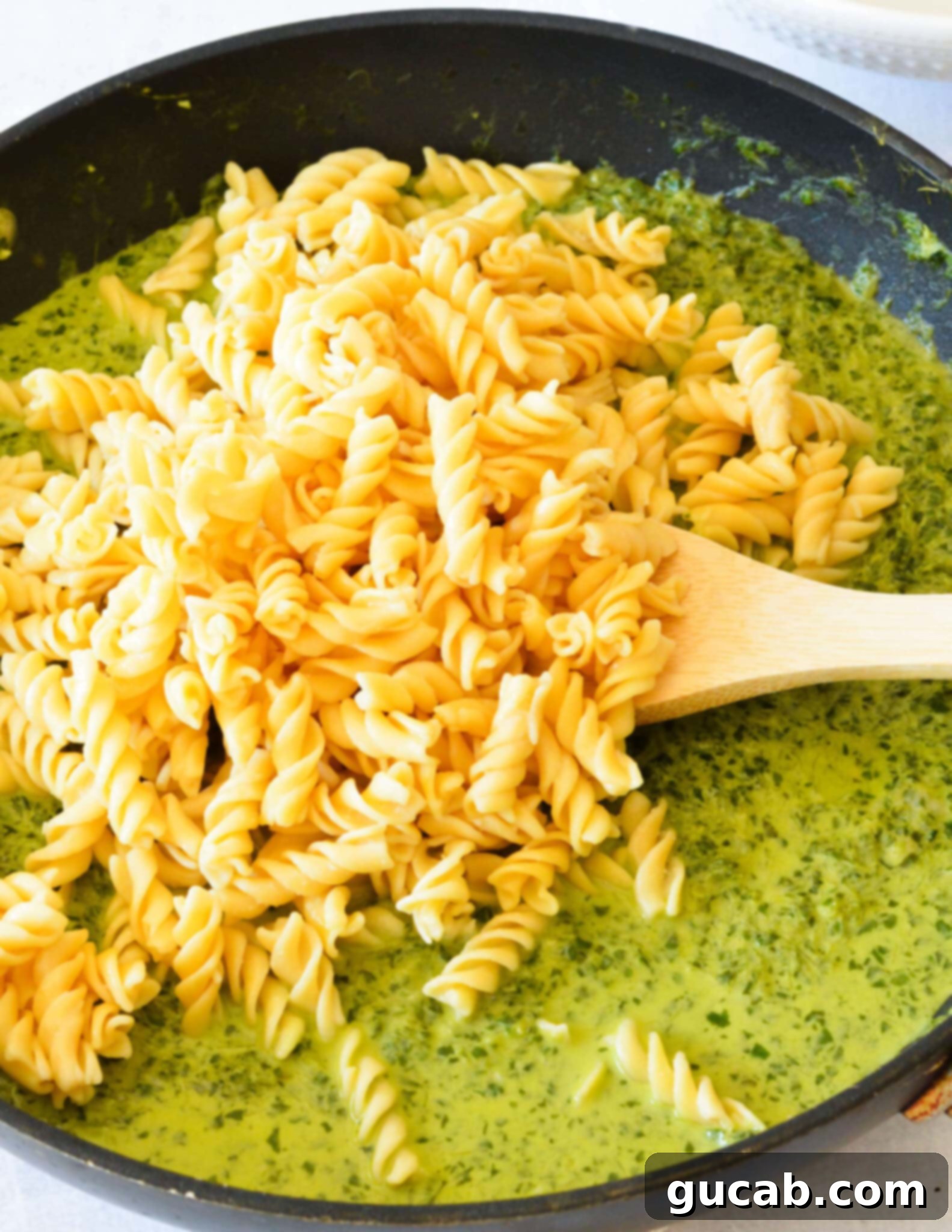 Cooked pasta perfectly tossed in the vibrant, creamy kale sauce within a large skillet, ready to be served.