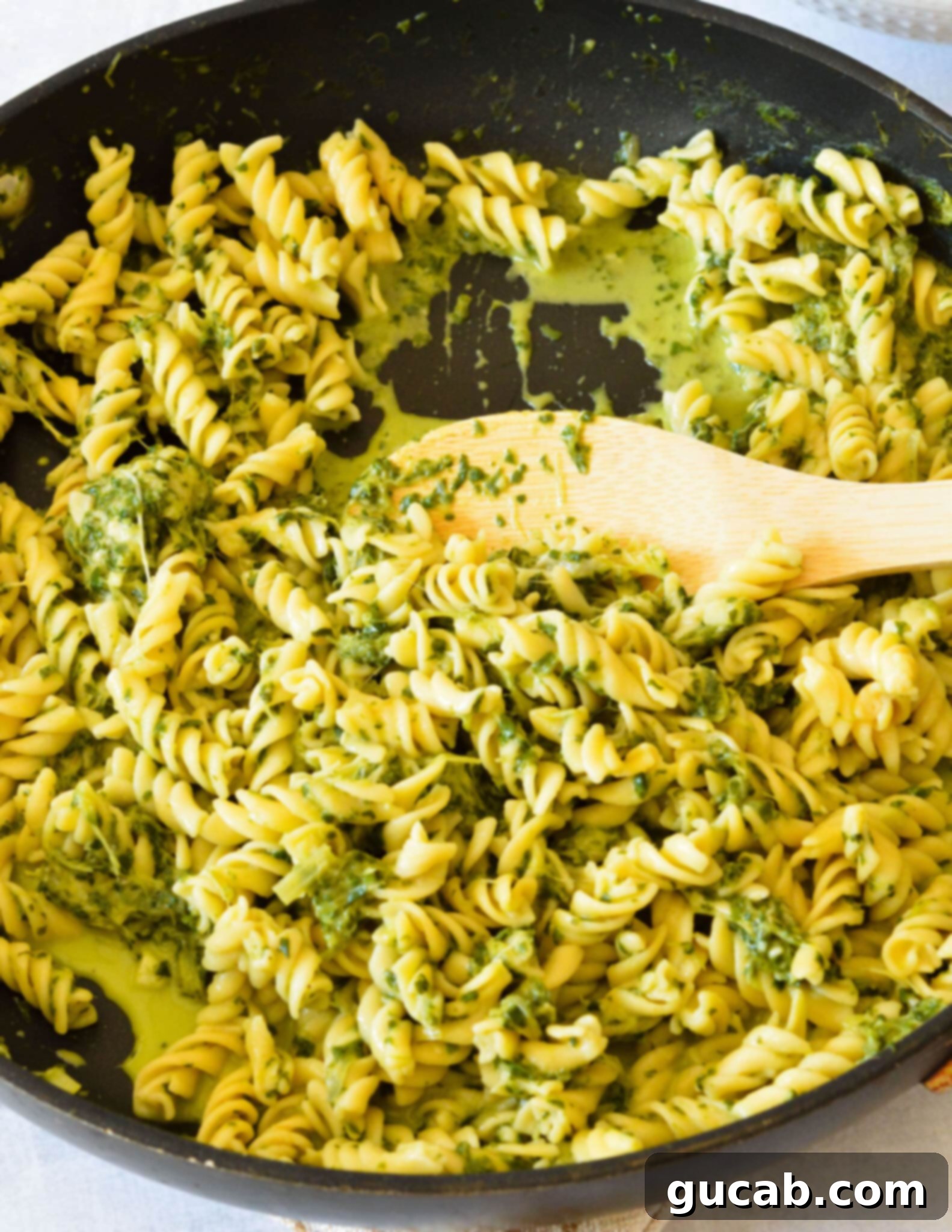 A large nonstick skillet filled with creamy kale pasta, being gently stirred with a wooden spoon, ready for serving.