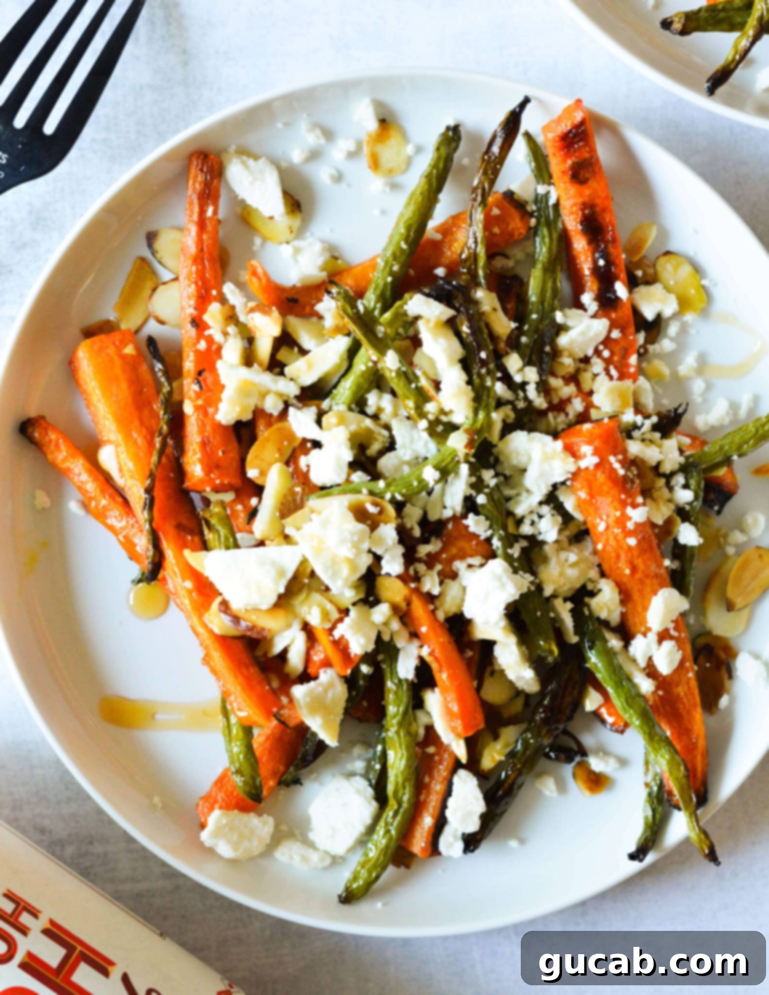 A vibrant plate featuring perfectly roasted green beans and carrots, generously topped with crumbled feta cheese, golden toasted almonds, and a glistening drizzle of hot honey.