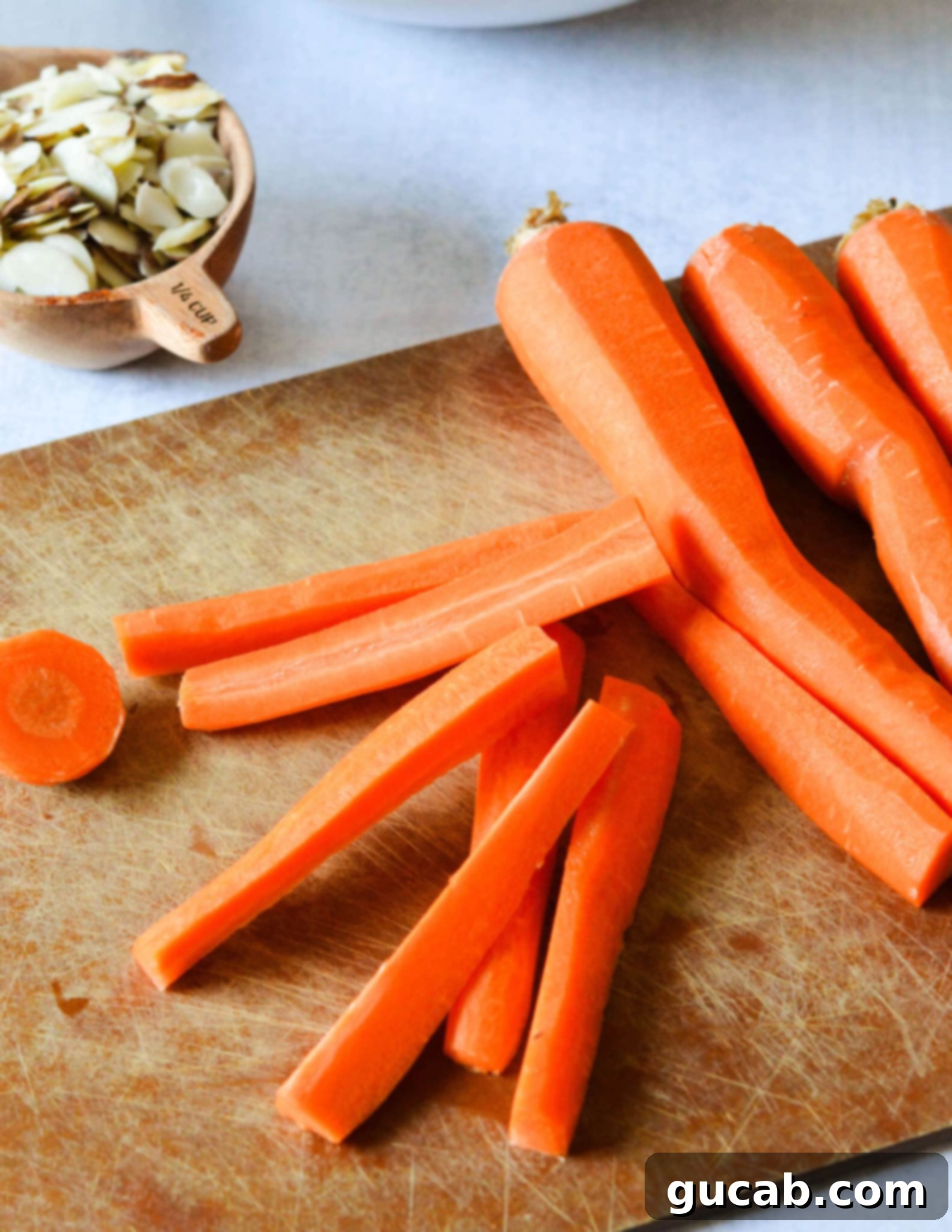 Neatly sliced carrots, uniform in size, arranged on a rustic wooden cutting board, ready for preparation.