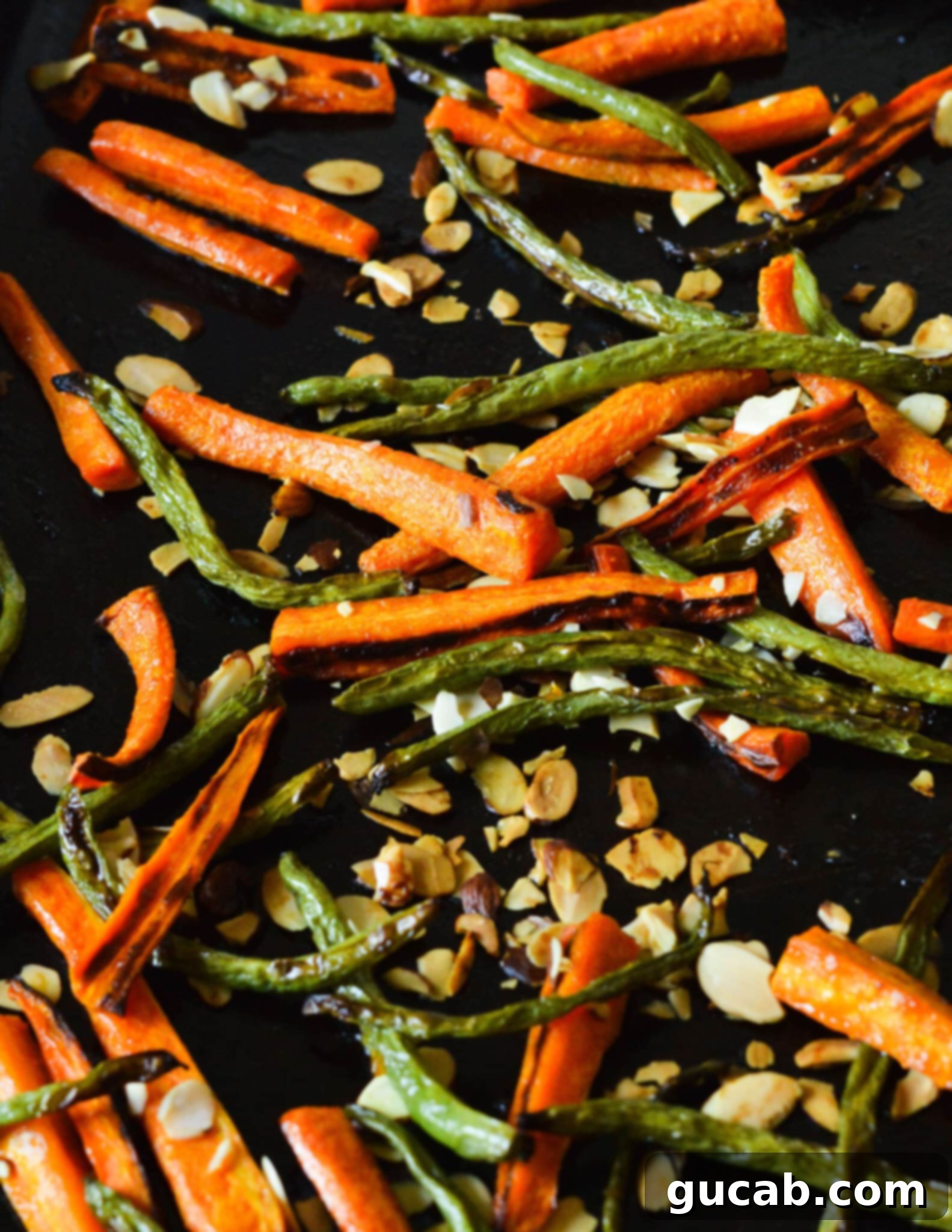 Crisp roasted carrots and green beans, beautifully caramelized, with golden toasted almonds scattered across the baking sheet, fresh from the oven.