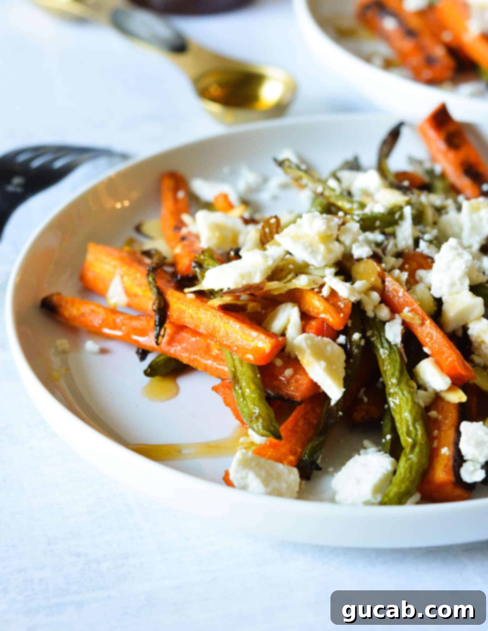 A serving dish brimming with roasted carrots and green beans, adorned with toasted almonds, crumbled feta, and a finishing drizzle of hot honey, ready to be enjoyed.