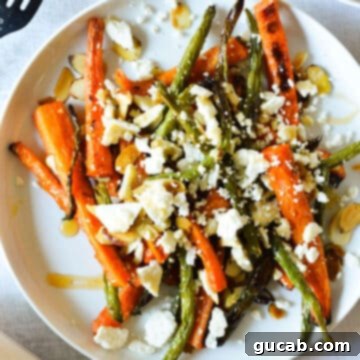A tantalizing image of roasted carrots and green beans on a plate, adorned with crumbled feta, toasted almonds, and a drizzle of hot honey, highlighting its deliciousness.