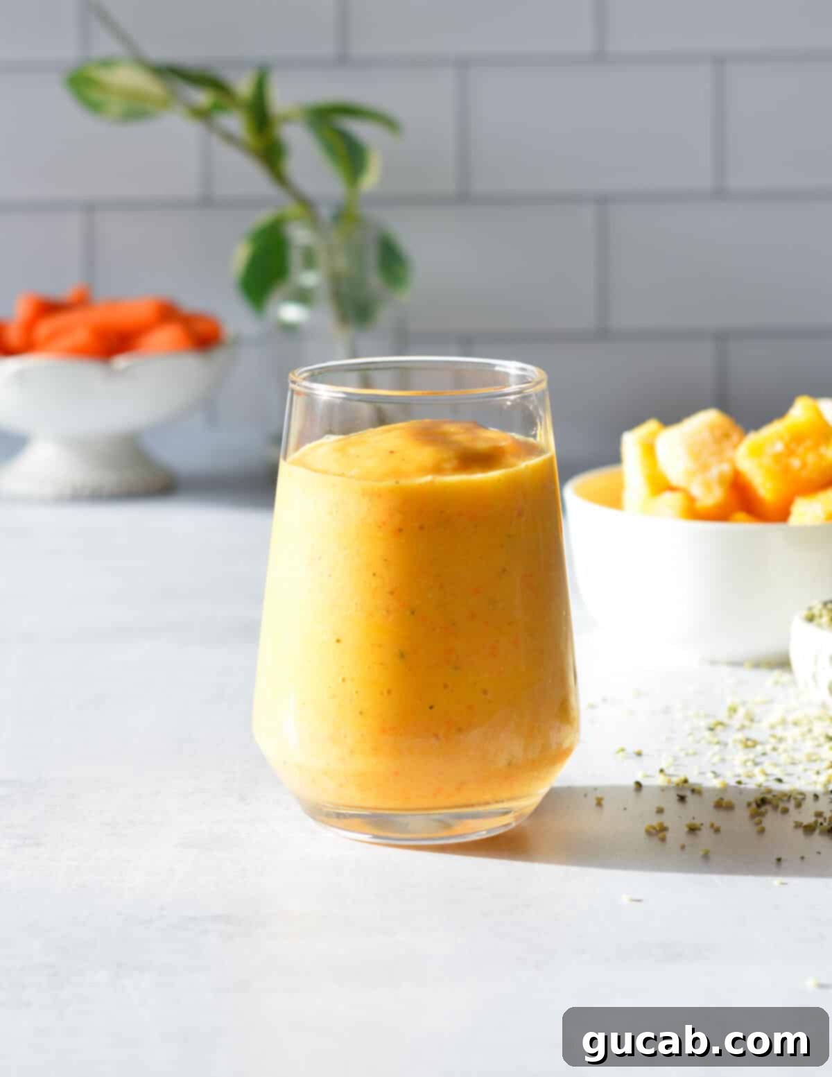 Vibrant orange carrot banana smoothie in a glass with a straw, showcasing its refreshing texture and inviting color.