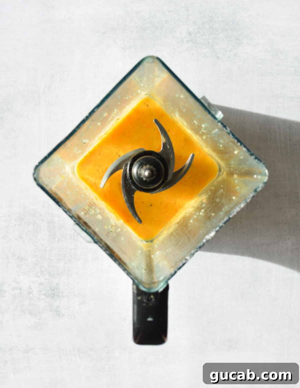 The carrot banana smoothie is actively blending in a high-speed blender, showing the vibrant orange mixture in motion.