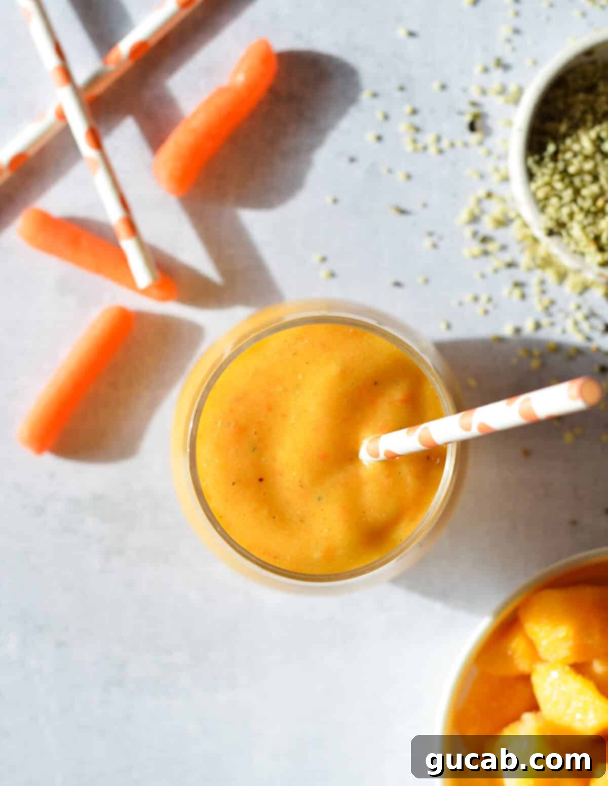 Close-up aerial view of a vibrant carrot banana smoothie in a glass, highlighting its smooth, inviting texture and rich orange color.