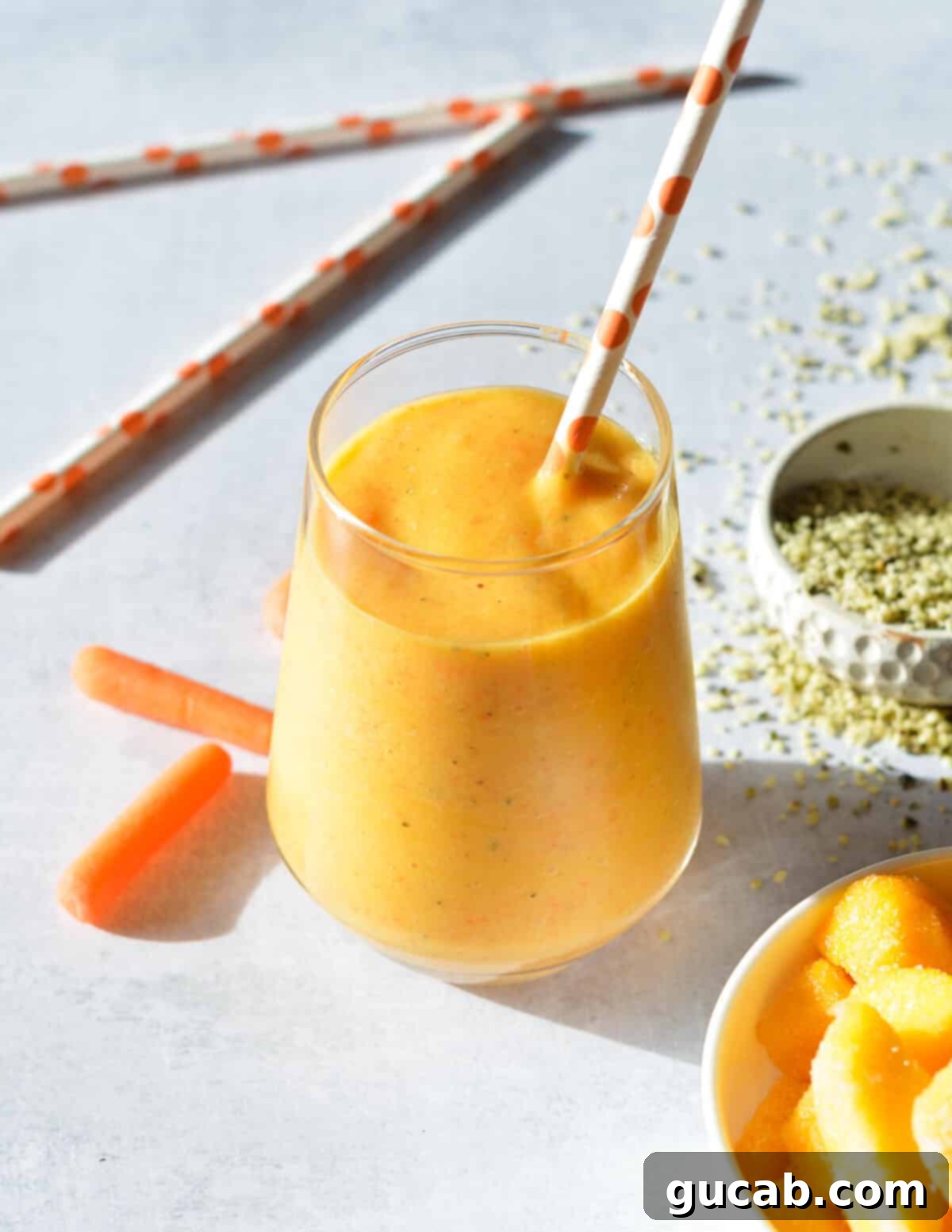A refreshing carrot banana smoothie in a clear glass next to a small bowl of hemp hearts, highlighting the healthy additions.