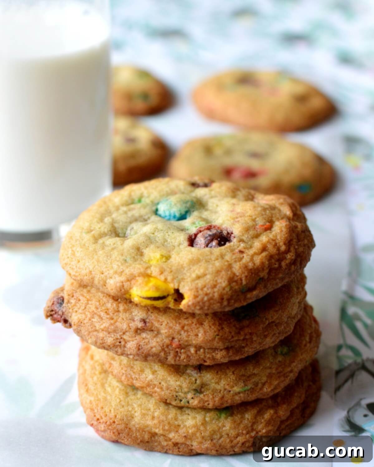 A close-up of a stack of freshly baked gluten-free M&M cookies, highlighting their soft texture and colorful chocolate candies.