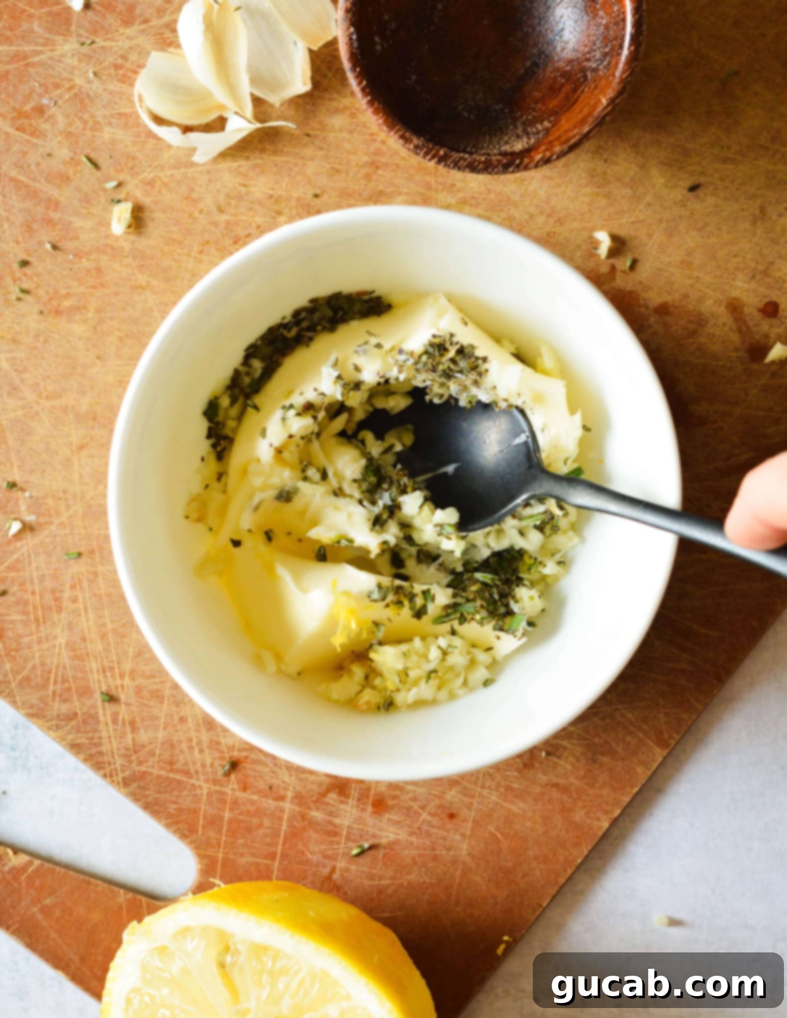A bowl containing a mix of dried basil, minced rosemary, minced garlic, and lemon zest, ready to be added to butter.