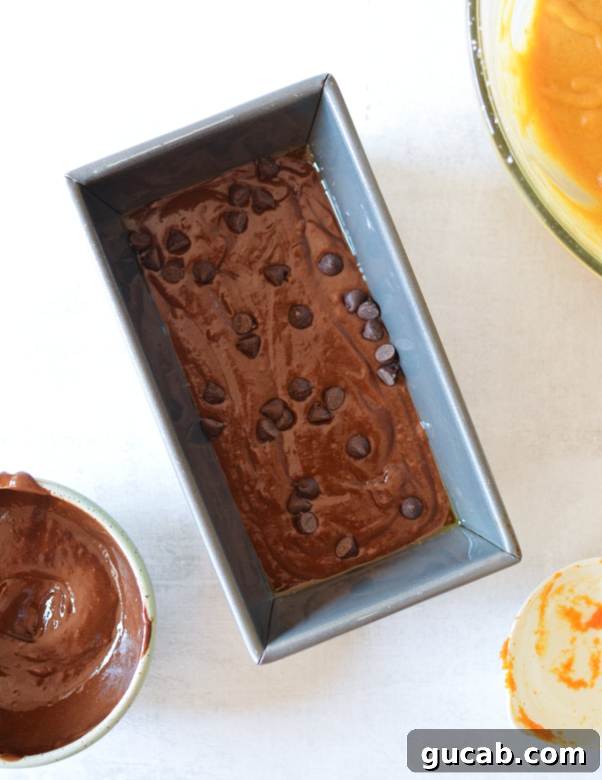 The first layer of chocolate batter, sprinkled with chocolate chips, in a loaf pan.