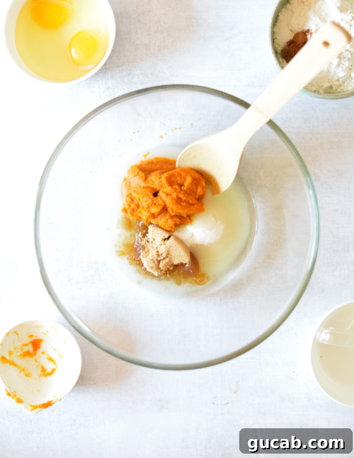 A bowl containing pumpkin puree, granulated sugar, brown sugar, and vegetable oil, ready to be mixed.