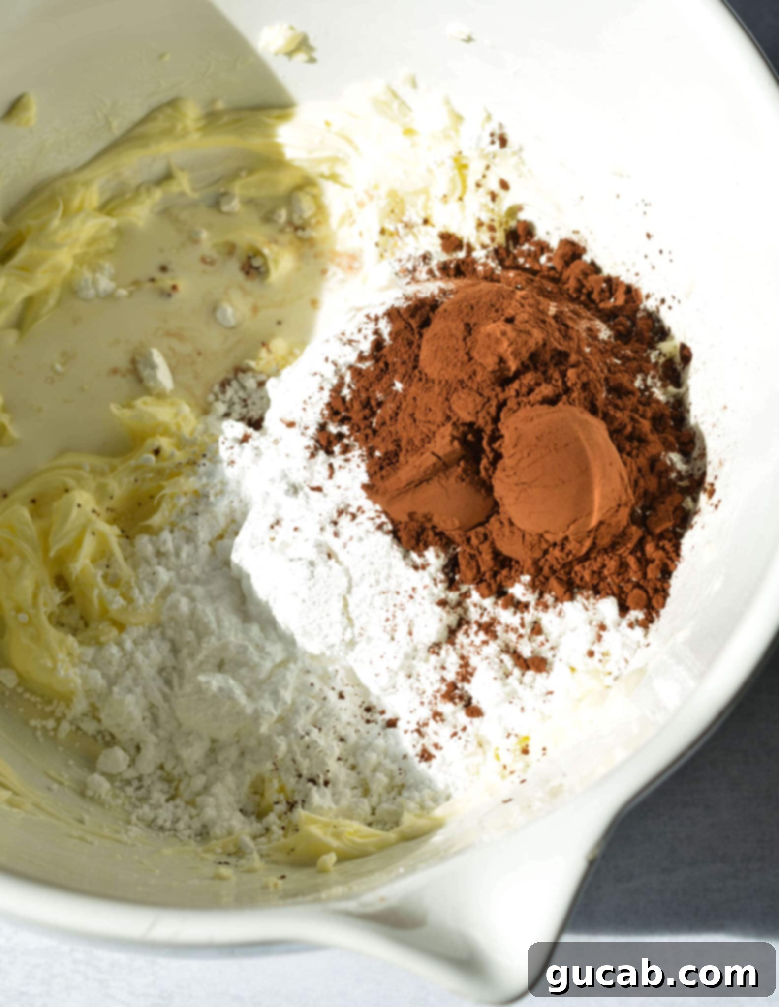 powdered sugar and cocoa powder in a bowl on top of creamed butter.