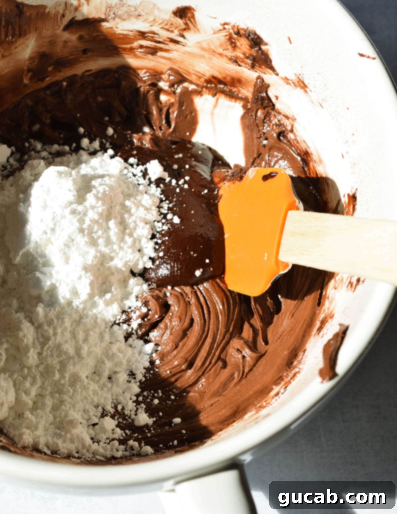 Fluffy Gluten-Free Chocolate Cupcakes 13 Chocolate frosting in a bowl with powdered sugar and cooled ganache on top, mid-preparation.
