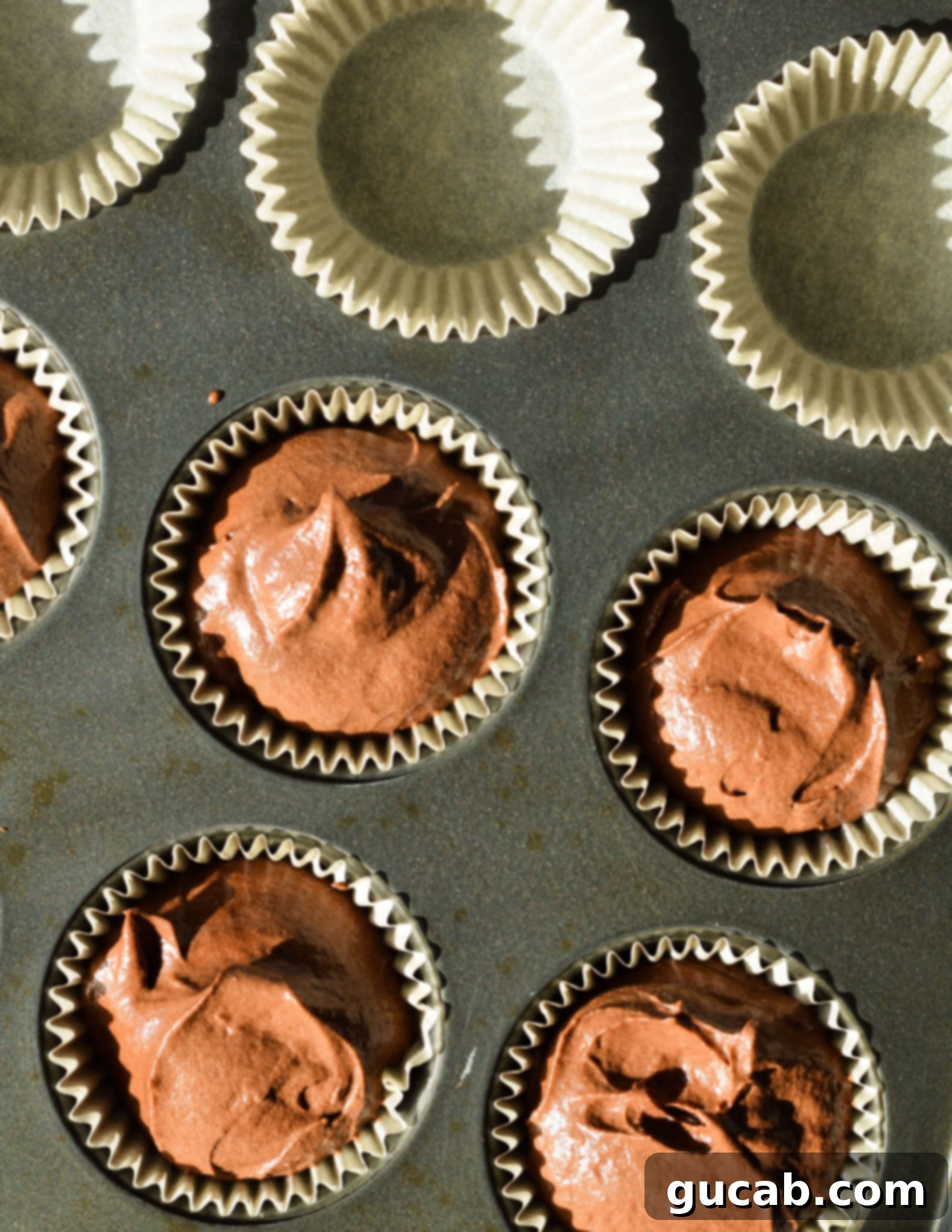 chocolate cake batter in muffin liners in a cupcake tin.
