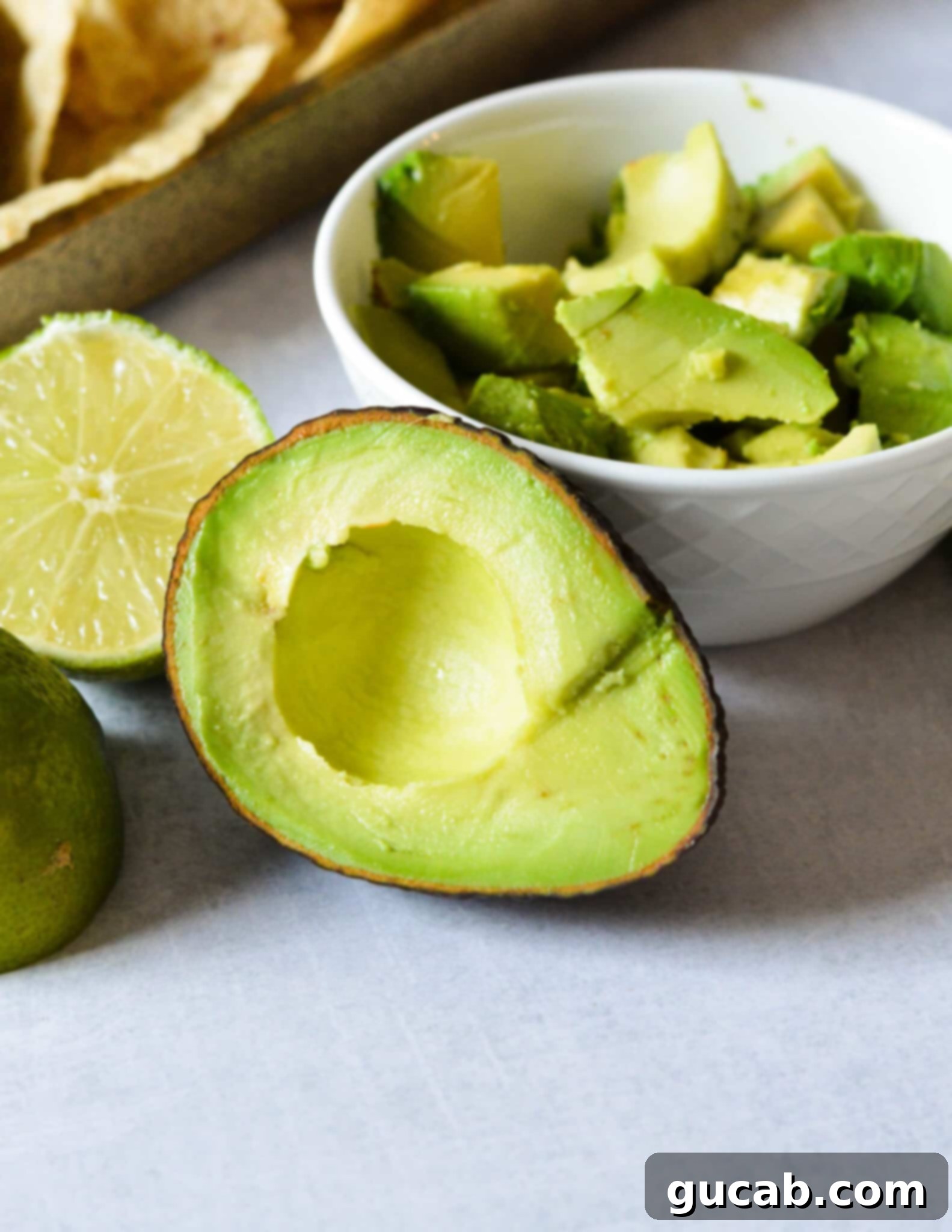 A bowl of perfectly diced, ripe avocado sits next to a half avocado, showcasing its creamy texture and vibrant green color, ready to be a delicious chili topping.