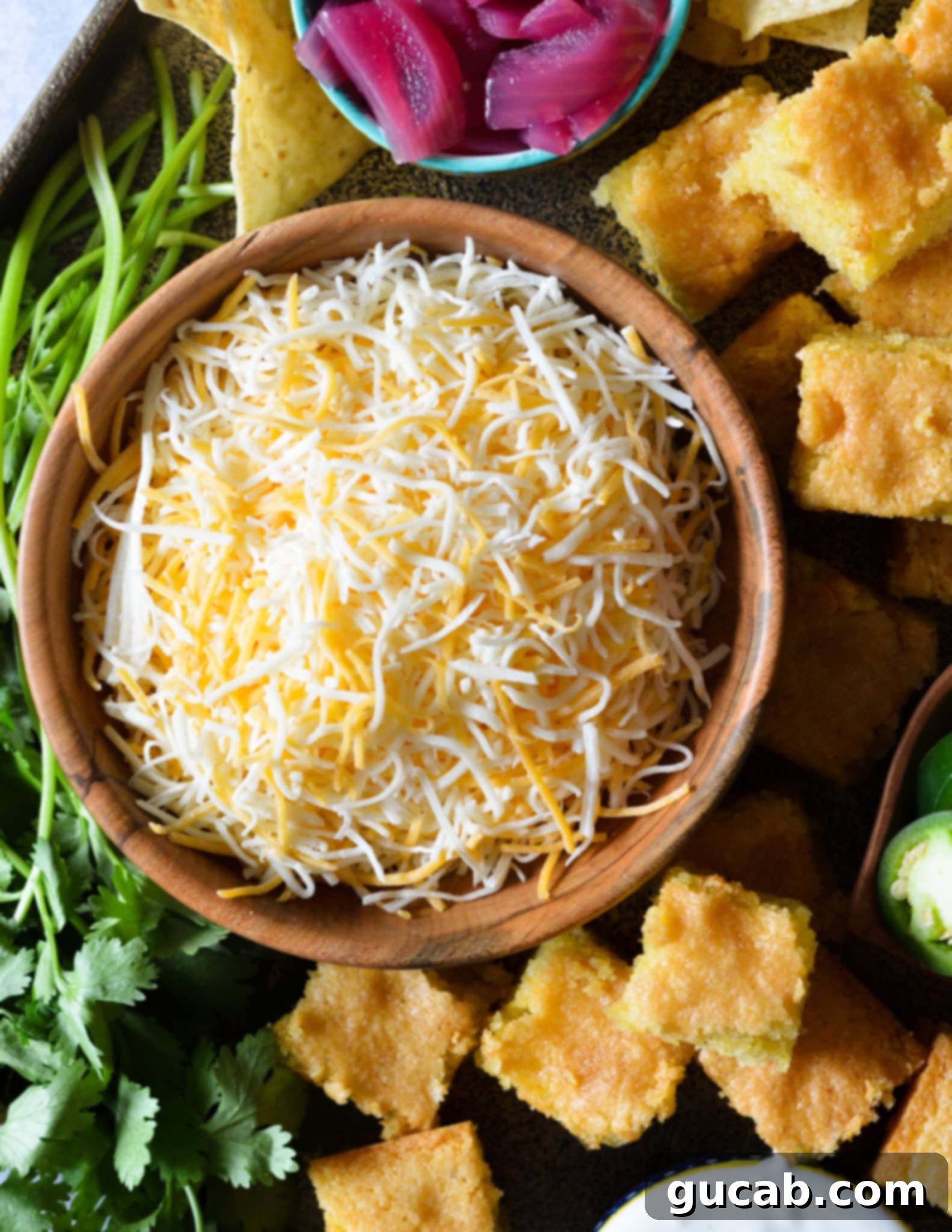 A beautifully arranged platter showcasing a bowl of shredded cheese, fluffy cornbread squares, and fresh cilantro sprigs, ready to complement a chili bar.