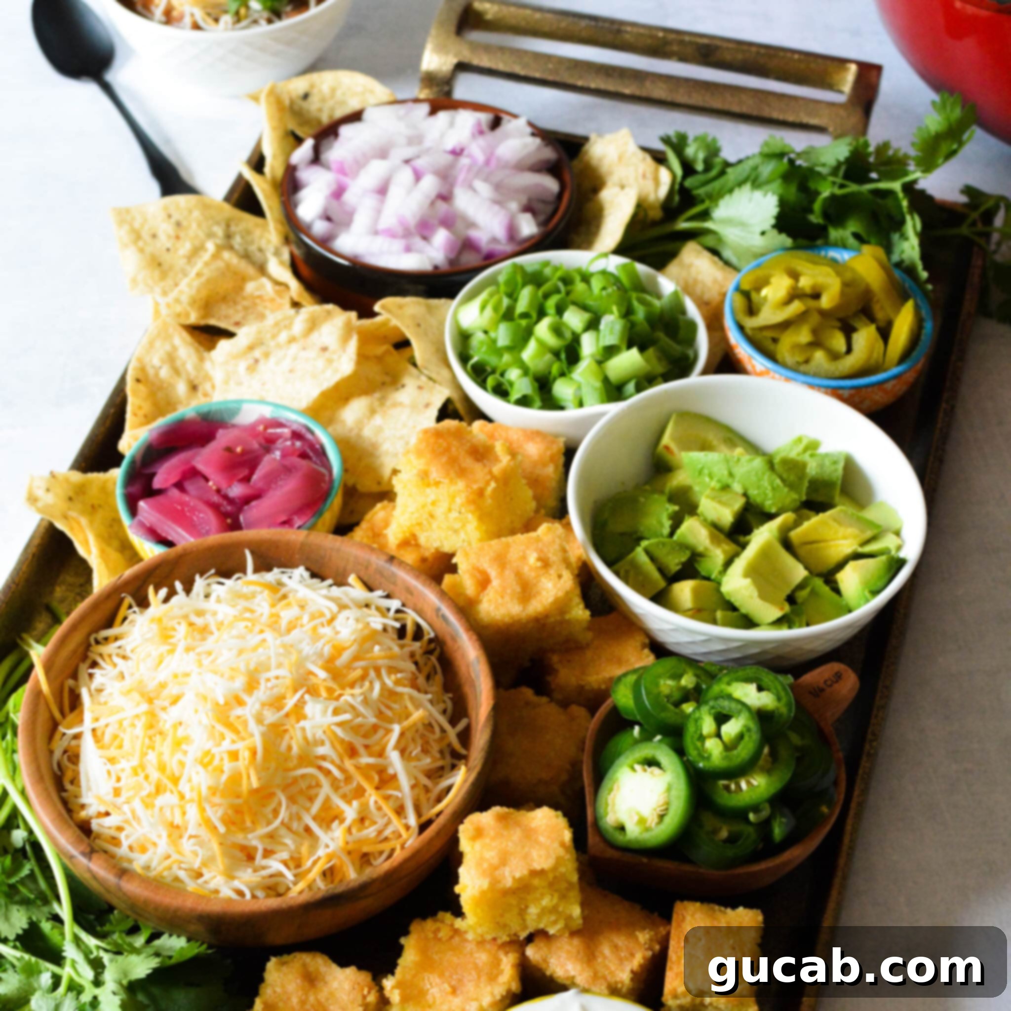 A selection of chili toppings neatly arranged in various bowls: diced red onion, sliced green onions, creamy diced avocado, tangy pickled red onions, spicy pickled jalapenos, rich shredded cheese, and fresh diced jalapenos.