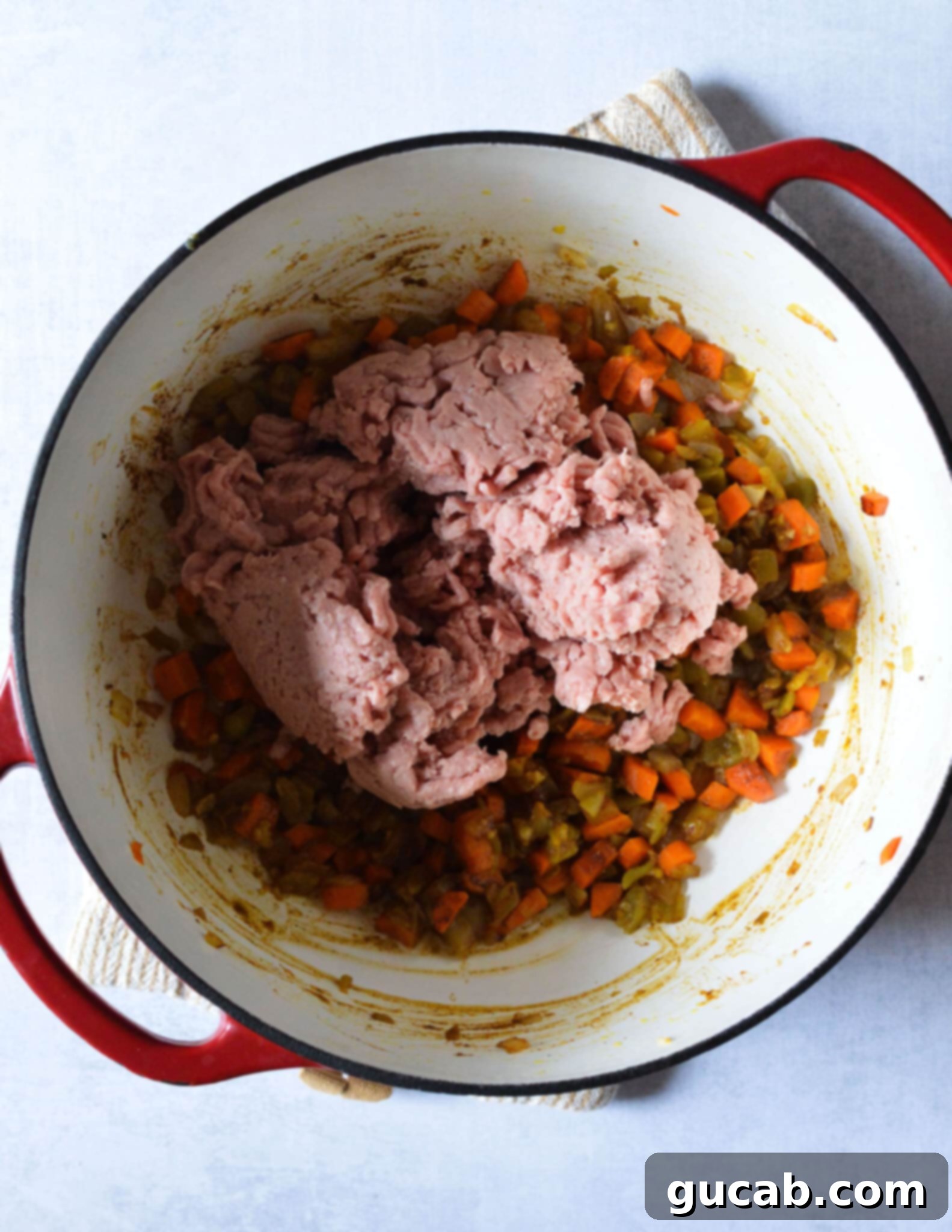 Raw ground turkey browning alongside sautéed vegetables in a Dutch oven.