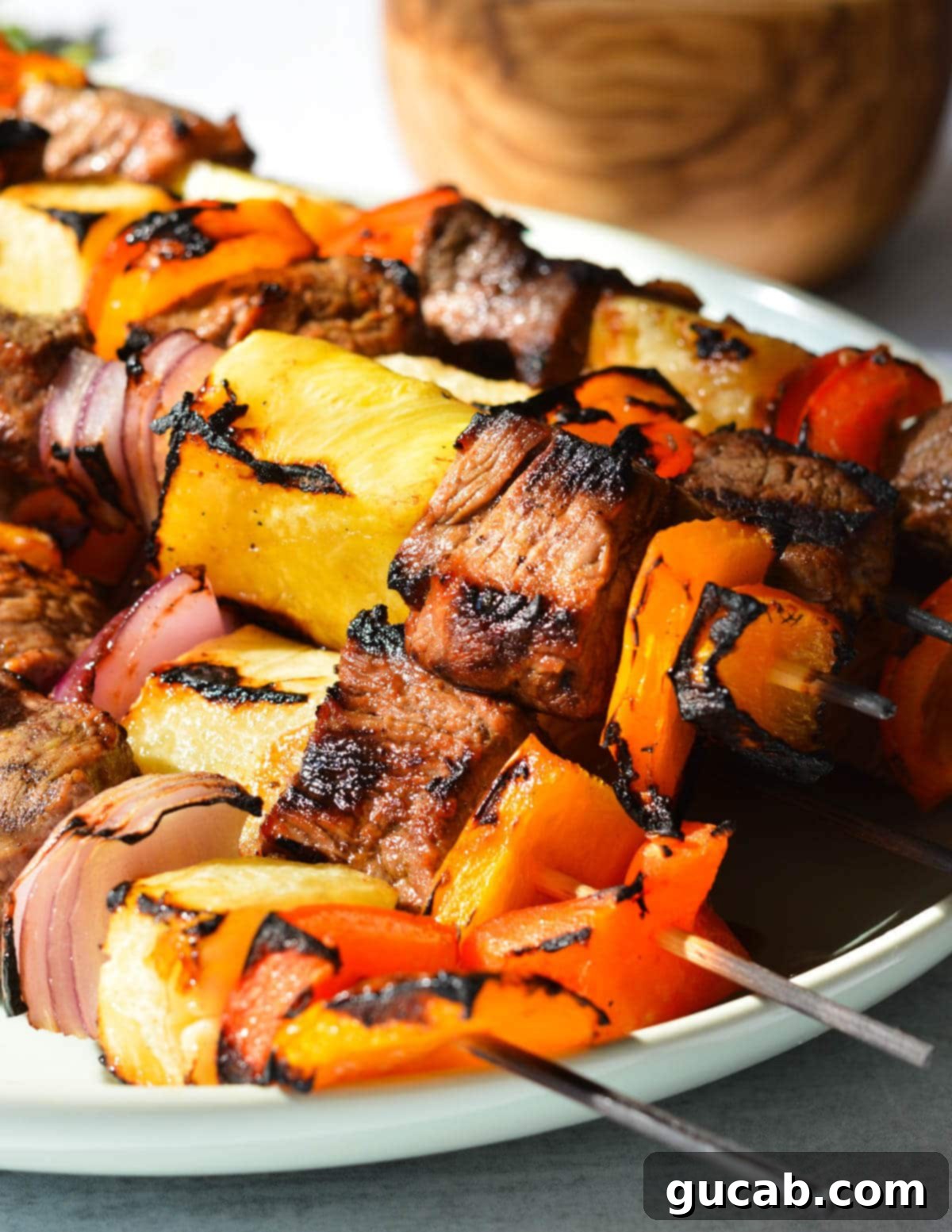 Grilled steak kebabs with pineapple, bell peppers, and red onion on a white plate, drizzled with chipotle sauce.