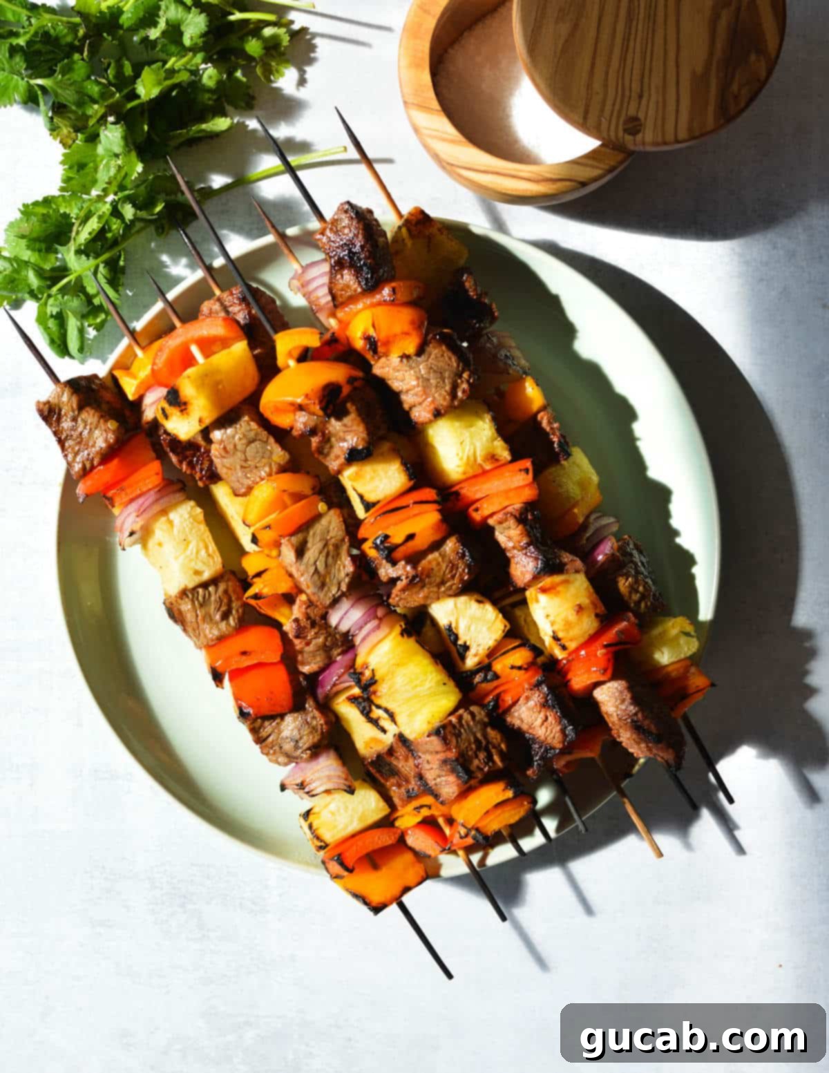 Cooked steak kebabs with grilled bell peppers, pineapple, and red onion on a white plate, ready to be served.