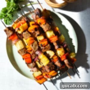 Steak kebabs with pineapple, bell peppers, and red onion on a plate, served with chipotle dipping sauce.