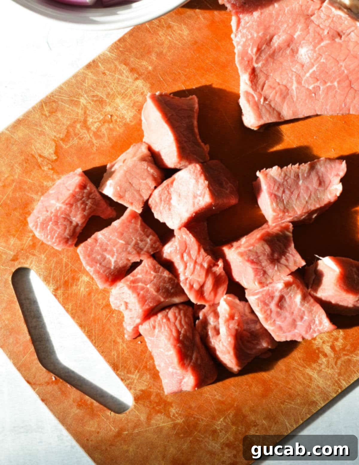 Sirloin steak cut into uniform chunks on a cutting board, ready for marinade.