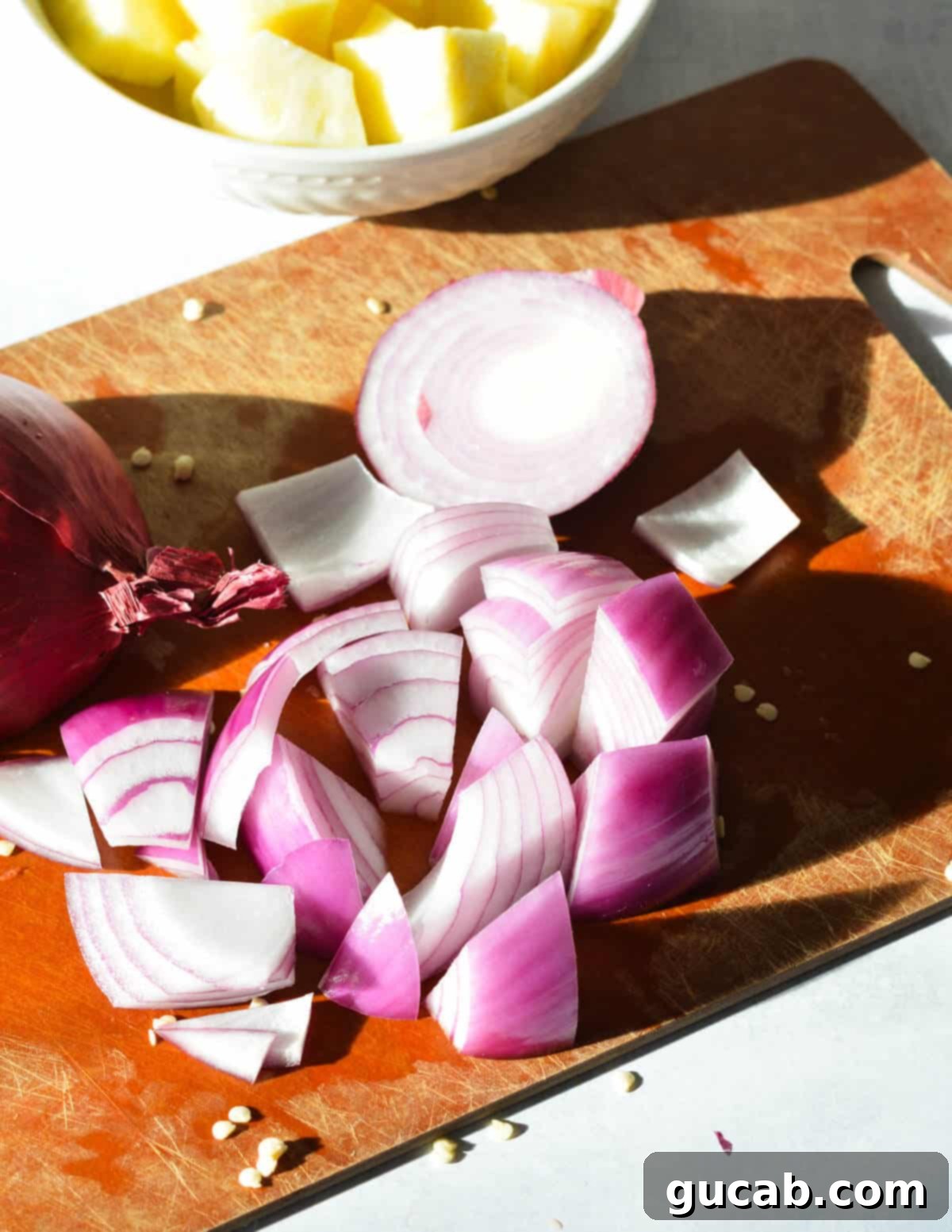 Red onion cut into large chunks on a cutting board, ready for skewering.