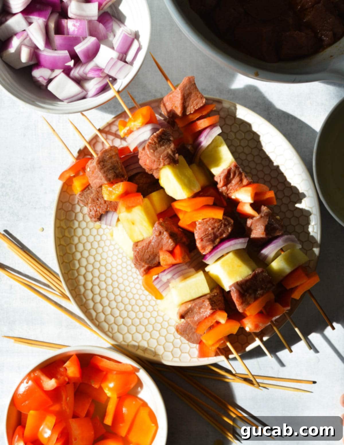 Uncooked steak, bell pepper, pineapple, and red onion kebabs assembled on a plate.