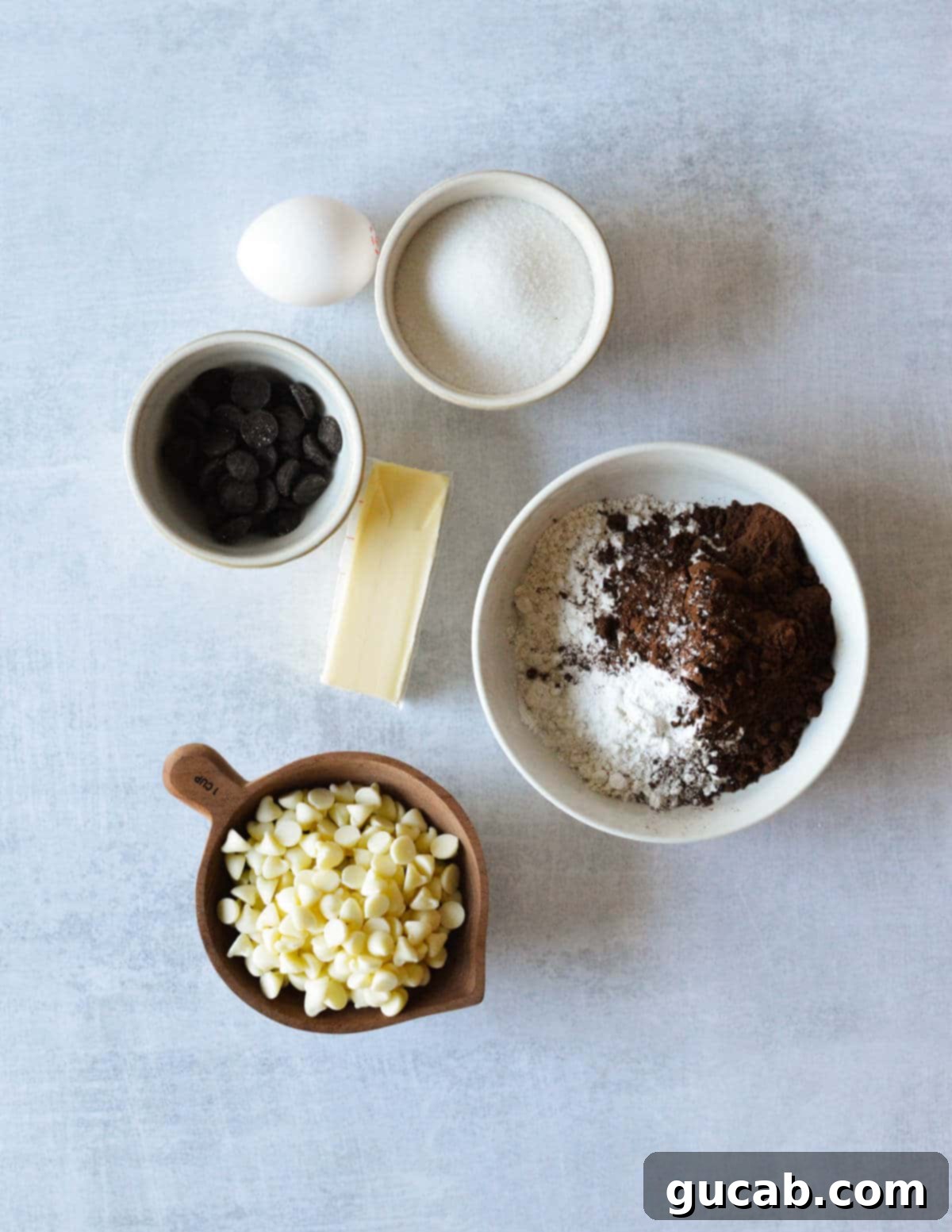 Key ingredients laid out for baking chocolate peppermint cookies: egg, sugar, premium dark chocolate chips, all-purpose flour, rich cocoa powder, sweet white chocolate chips, and softened butter.