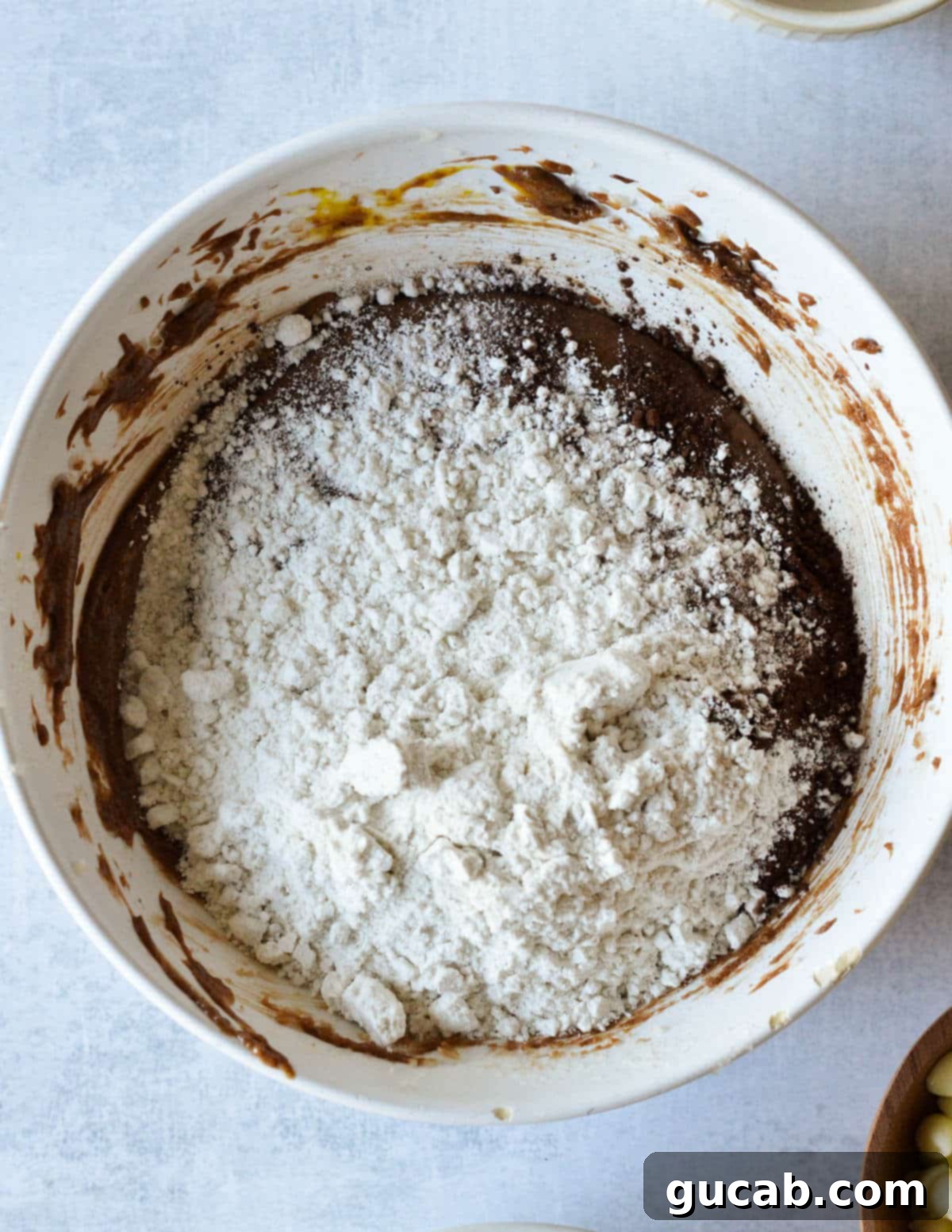 Chocolate cookie batter with dry ingredients, including flour, added on top, before mixing.