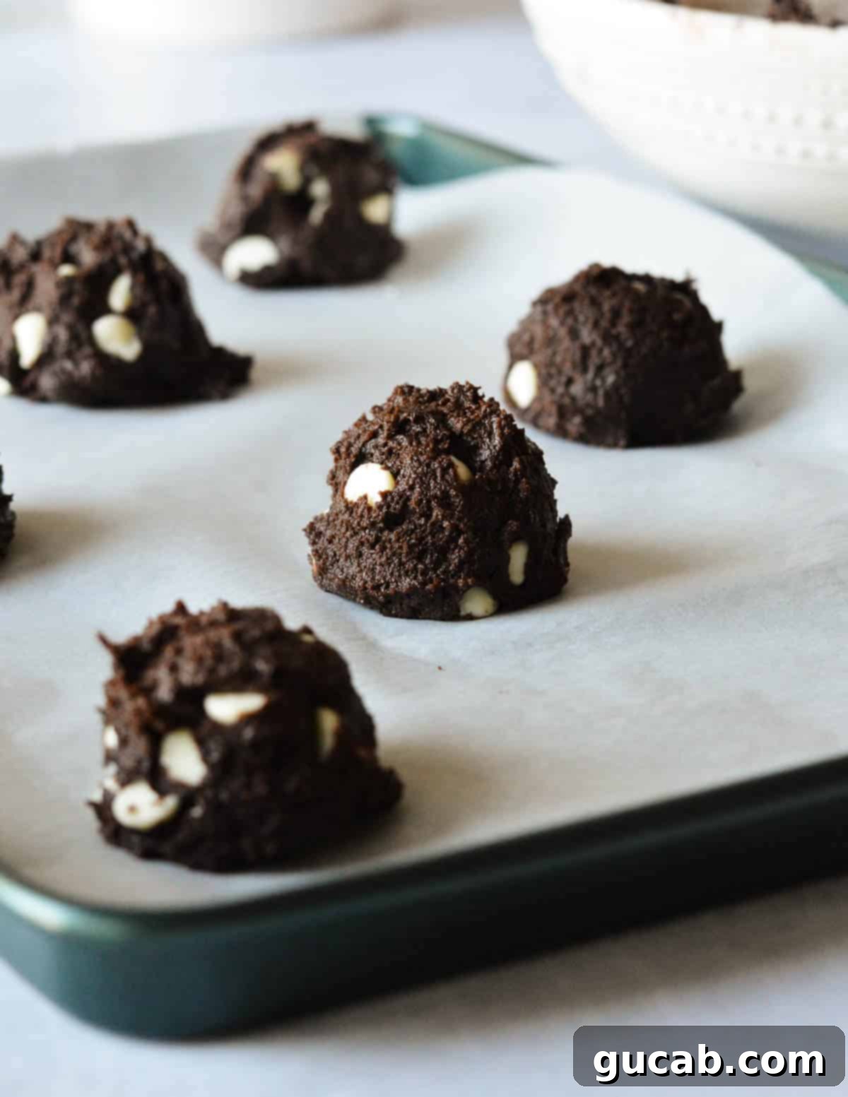 Portioned chocolate peppermint cookie dough balls arranged on a sheet pan, ready for baking.