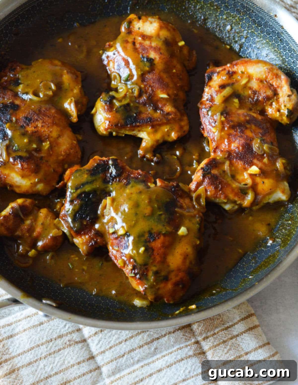 Mustard chicken thighs, perfectly seared and coated in sauce, presented in a rustic skillet, ready for serving.