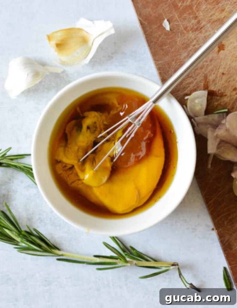 A close-up of a bowl containing yellow mustard, apricot jam, honey, garlic, shallots, and rosemary, the key ingredients for the sweet and tangy sauce.