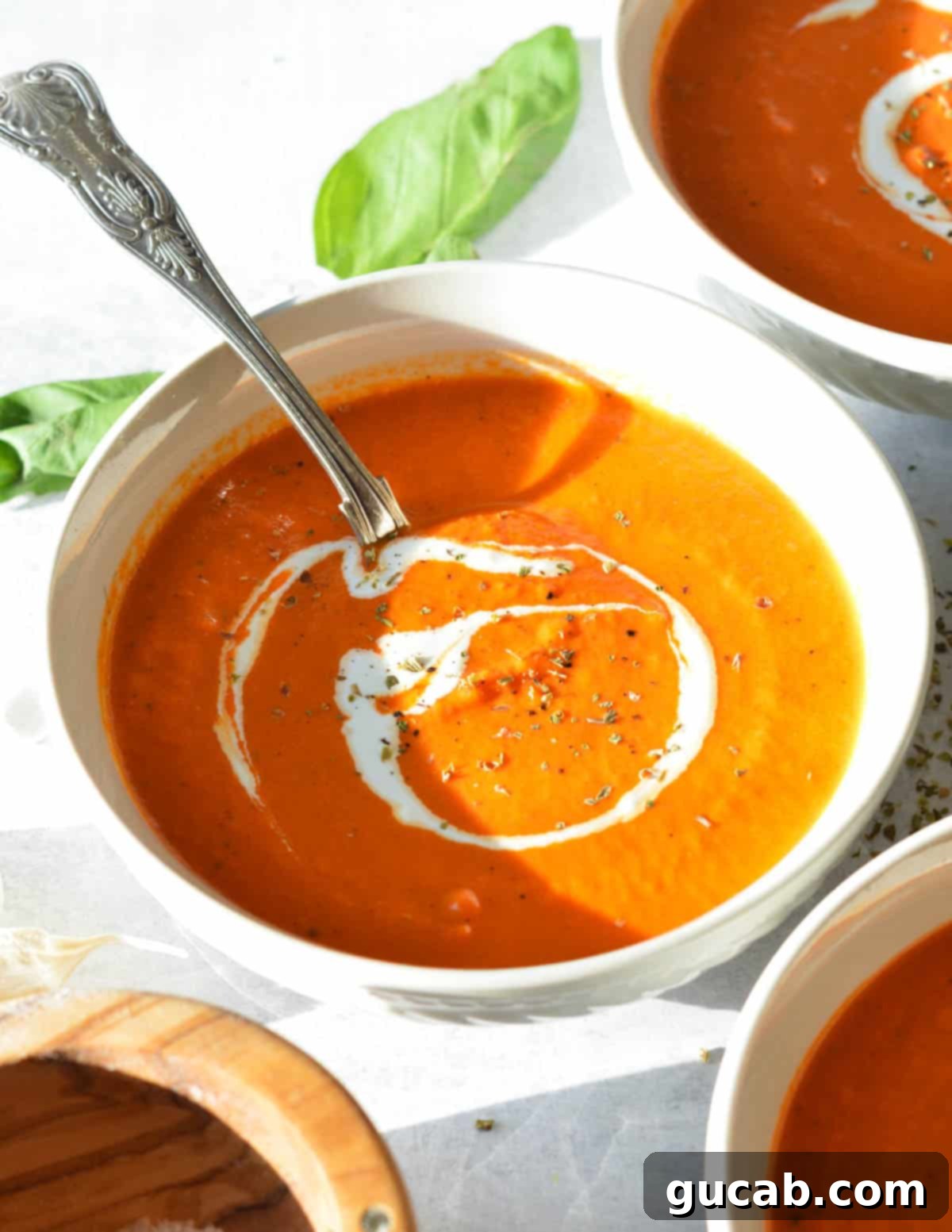 Roasted red pepper and tomato soup in a bowl with a spoon, garnished with fresh basil.