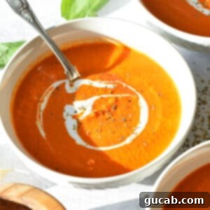 A bowl of creamy roasted red pepper and tomato soup, garnished with fresh basil.