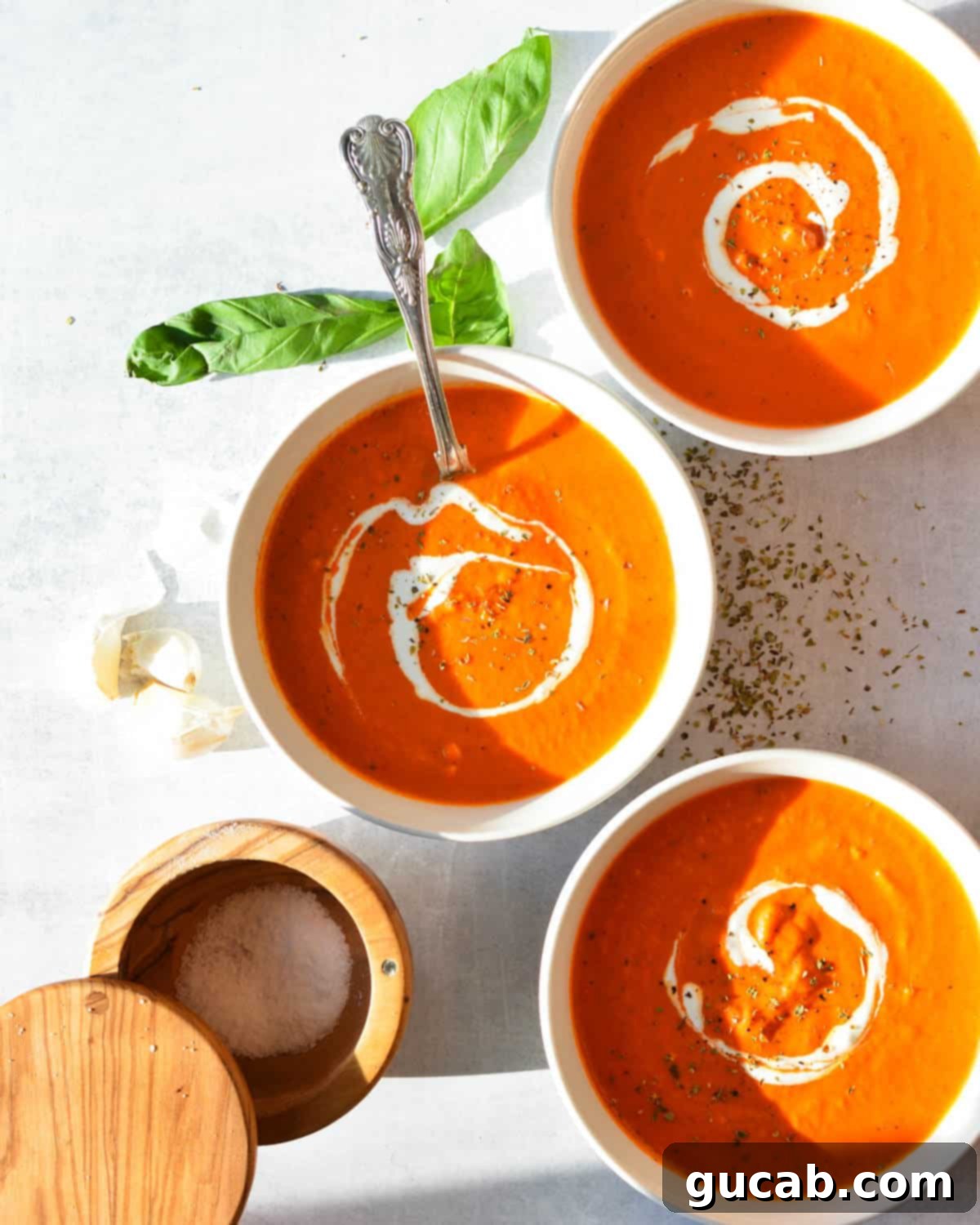 Three bowls of creamy roasted red pepper and tomato soup, garnished.