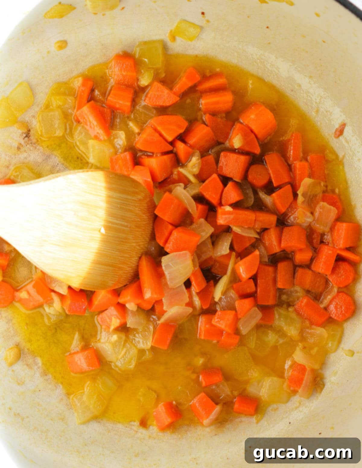 Diced carrots, diced onion, butter, and olive oil sautéing in a pot with a wooden spoon.