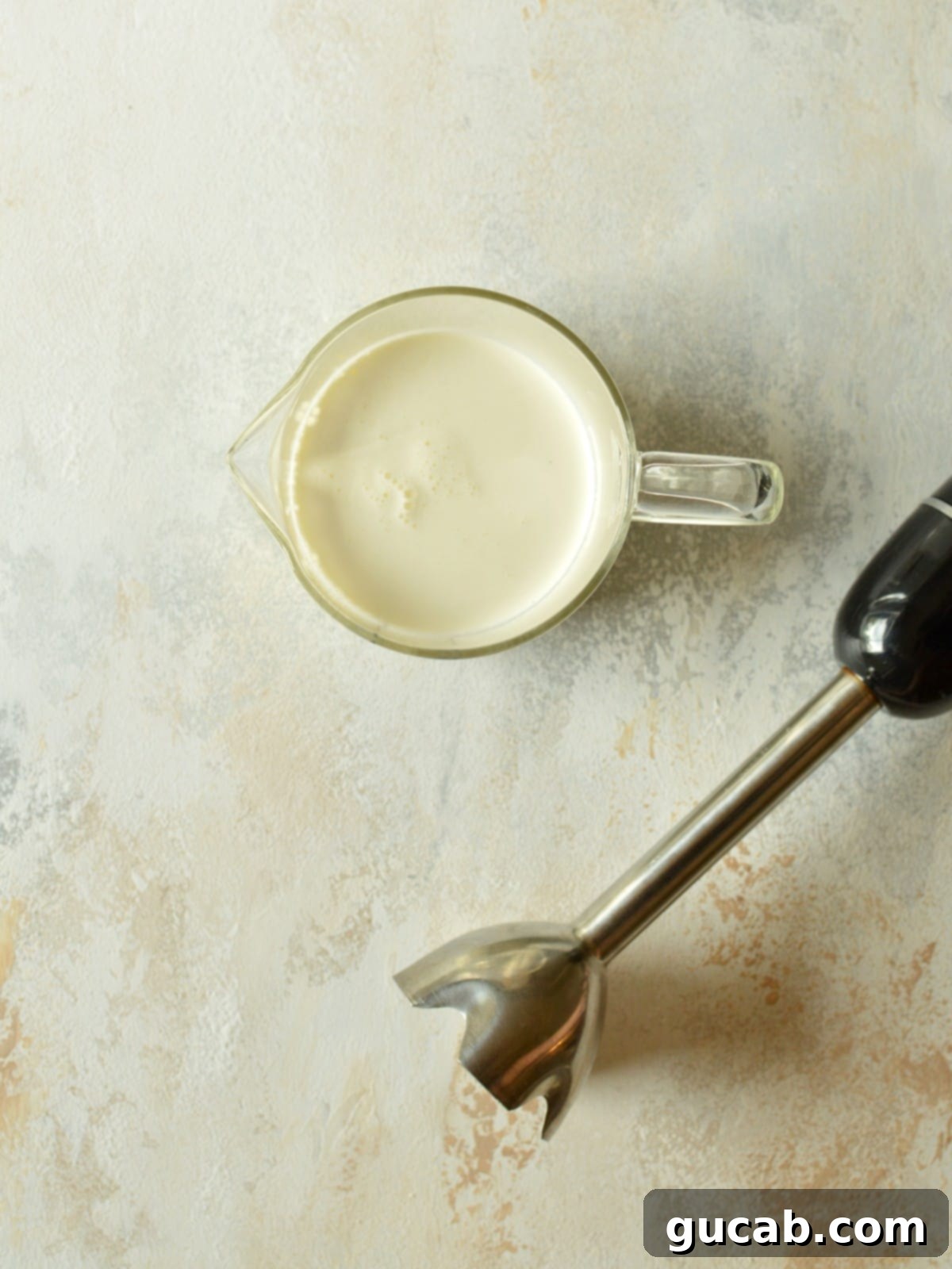 An immersion blender actively frothing sweet cream cold foam in a tall cup, illustrating the best method for a creamy texture.