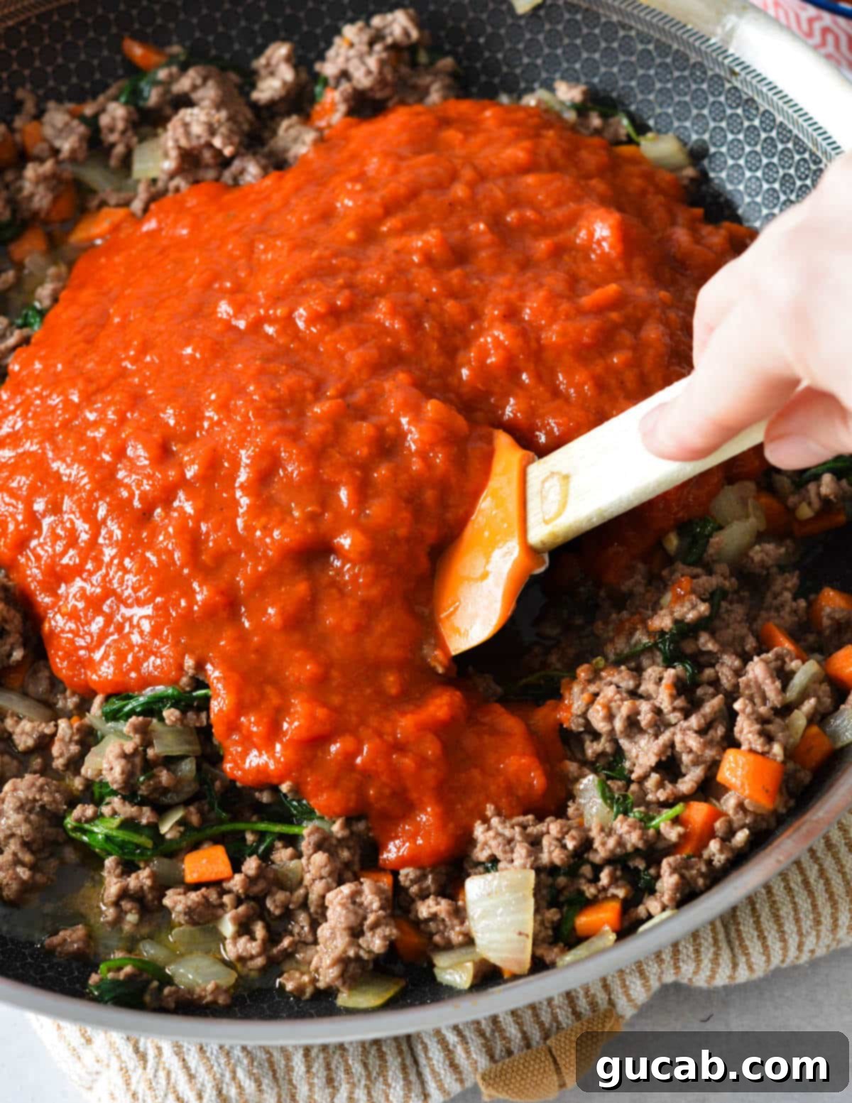 Marinara sauce added to the skillet on top of cooked ground beef and vegetables.