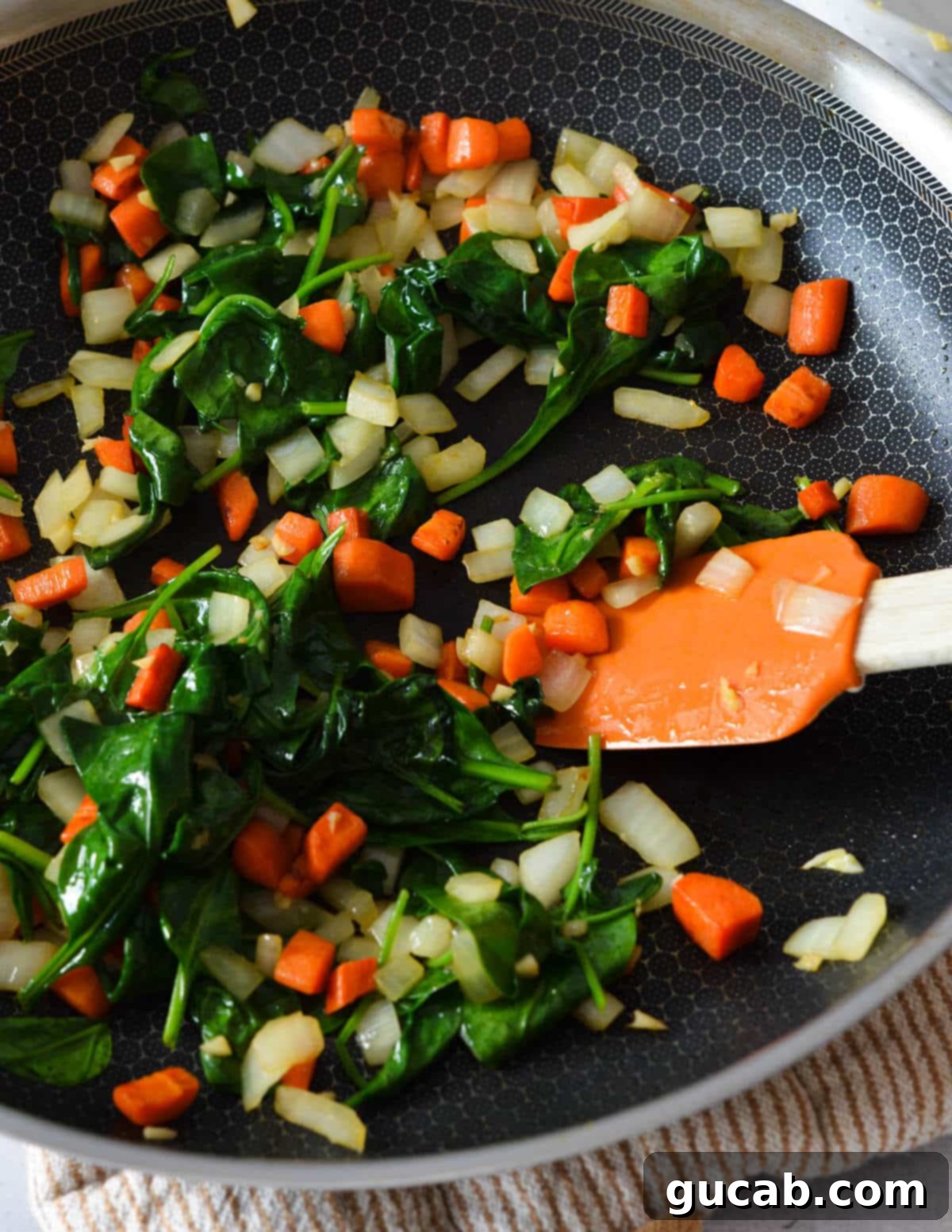 Sautéed carrots, onions, garlic, and baby spinach in a skillet, forming a colorful base for the meat sauce.