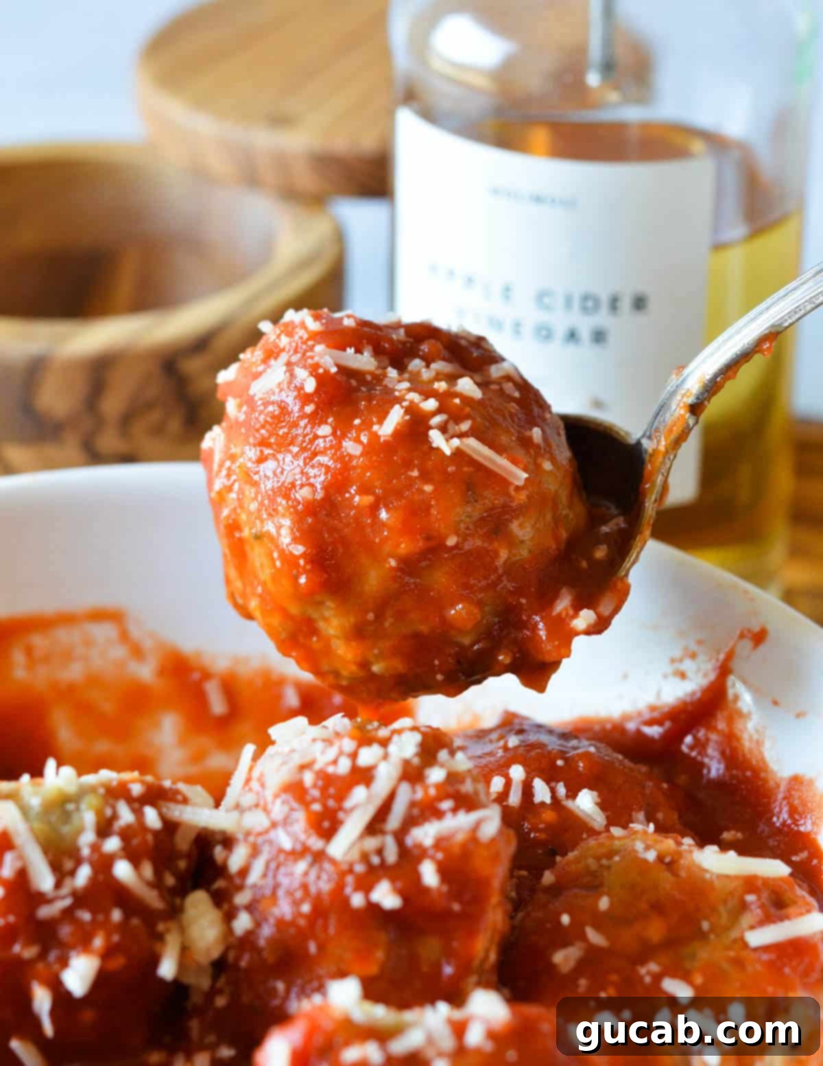 a spoon holding a meatball in marinara sauce. 