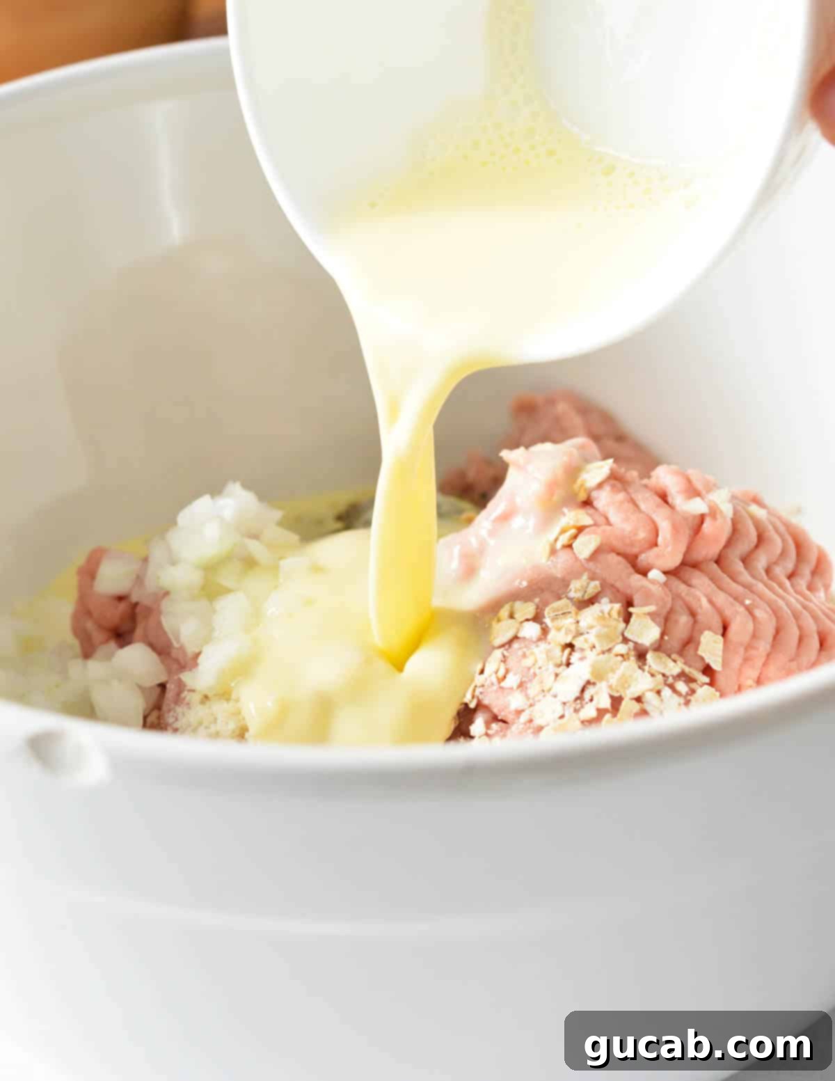 pouring milk and egg mixture into a bowl with ground turkey.