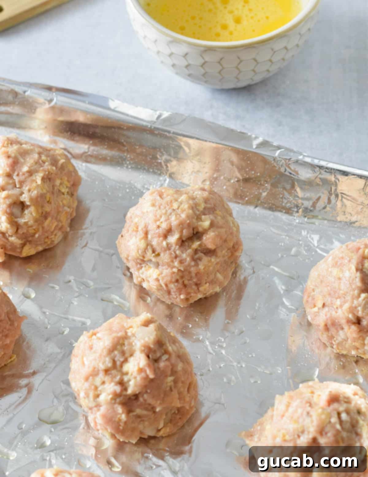 raw turkey meatballs on an aluminum foil lined sheet pan. 