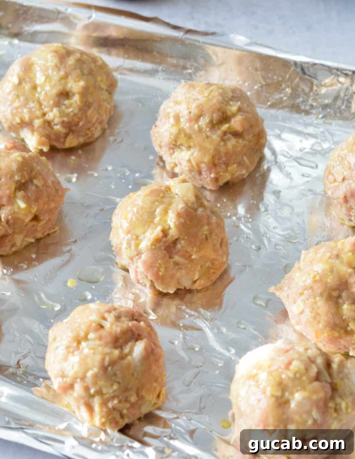 raw turkey meatballs coated in egg wash on a sheet pan. 