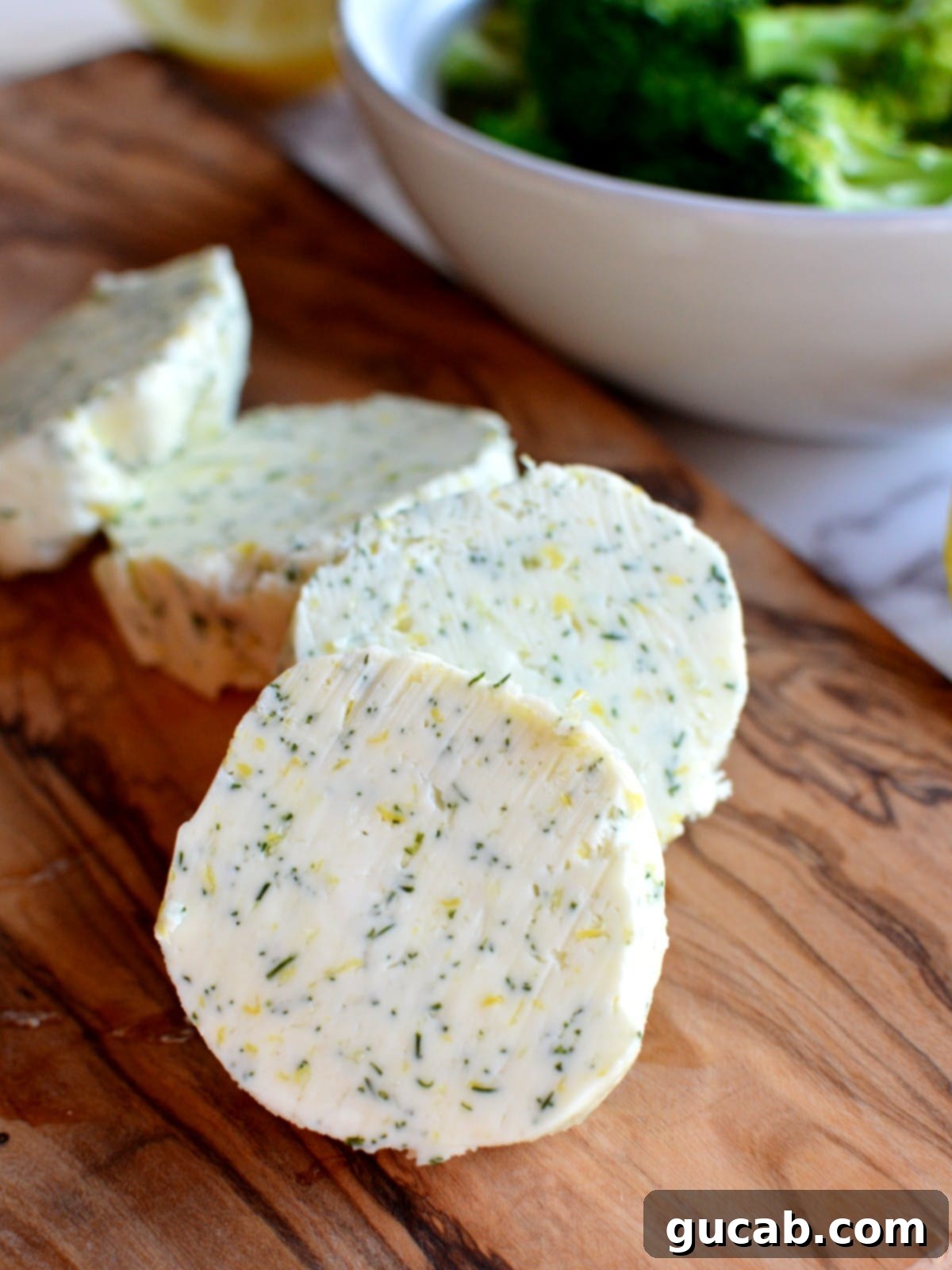 Close-up of a perfectly sliced disc of homemade dill butter, showcasing flecks of fresh green dill.